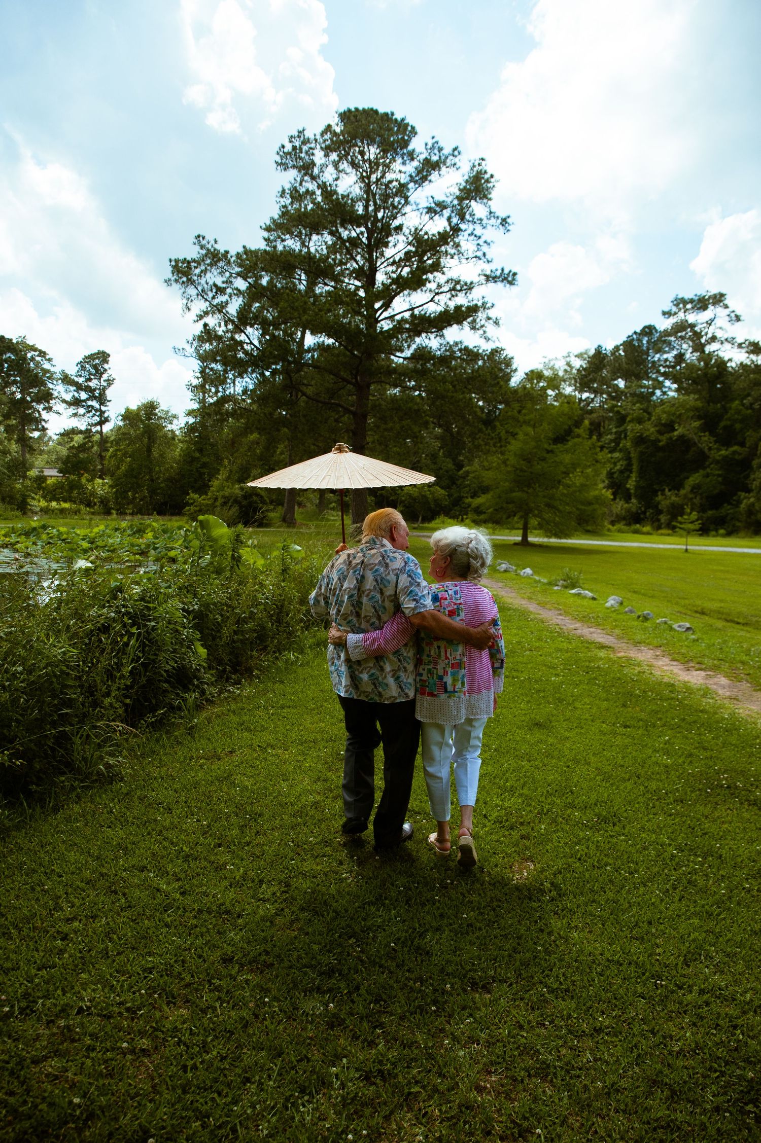A couple in floral prints walking together on a grassy hillside on a sunny day.