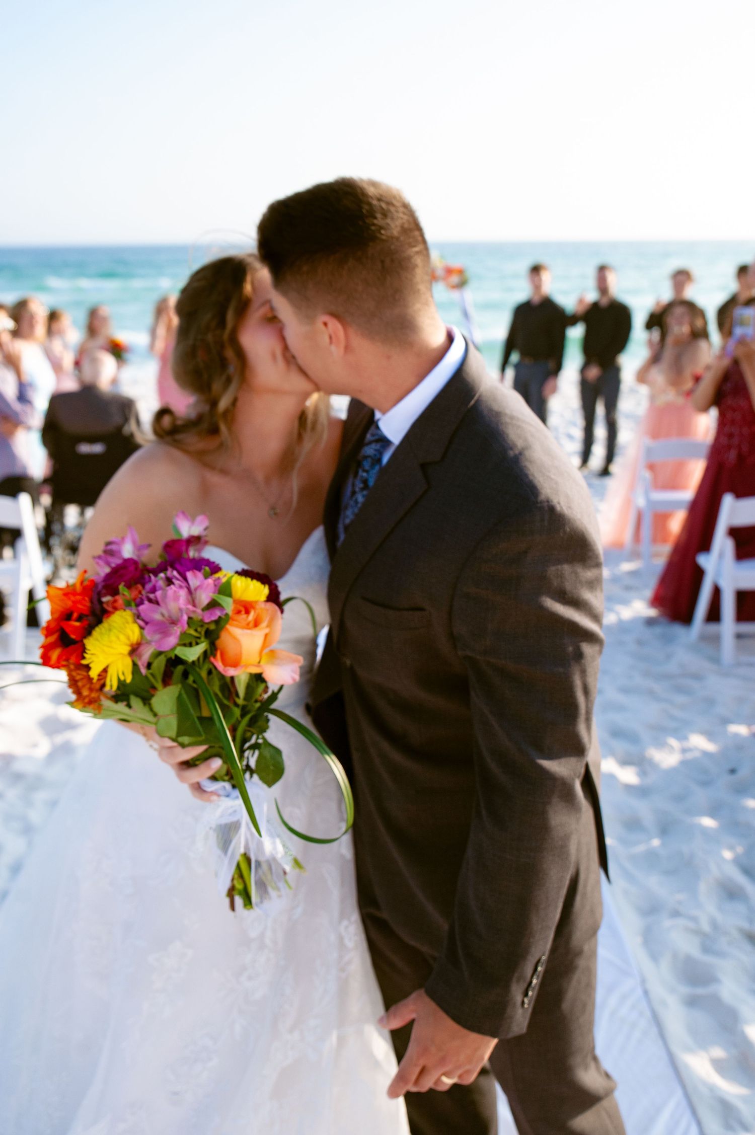 Newlyweds share a romantic kiss on a white sandy beach during their sunset wedding ceremony.