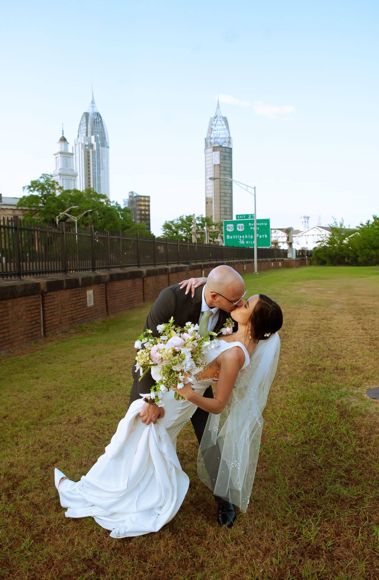 A dramatic wedding dip pose with Mobile's downtown skyline in the background.