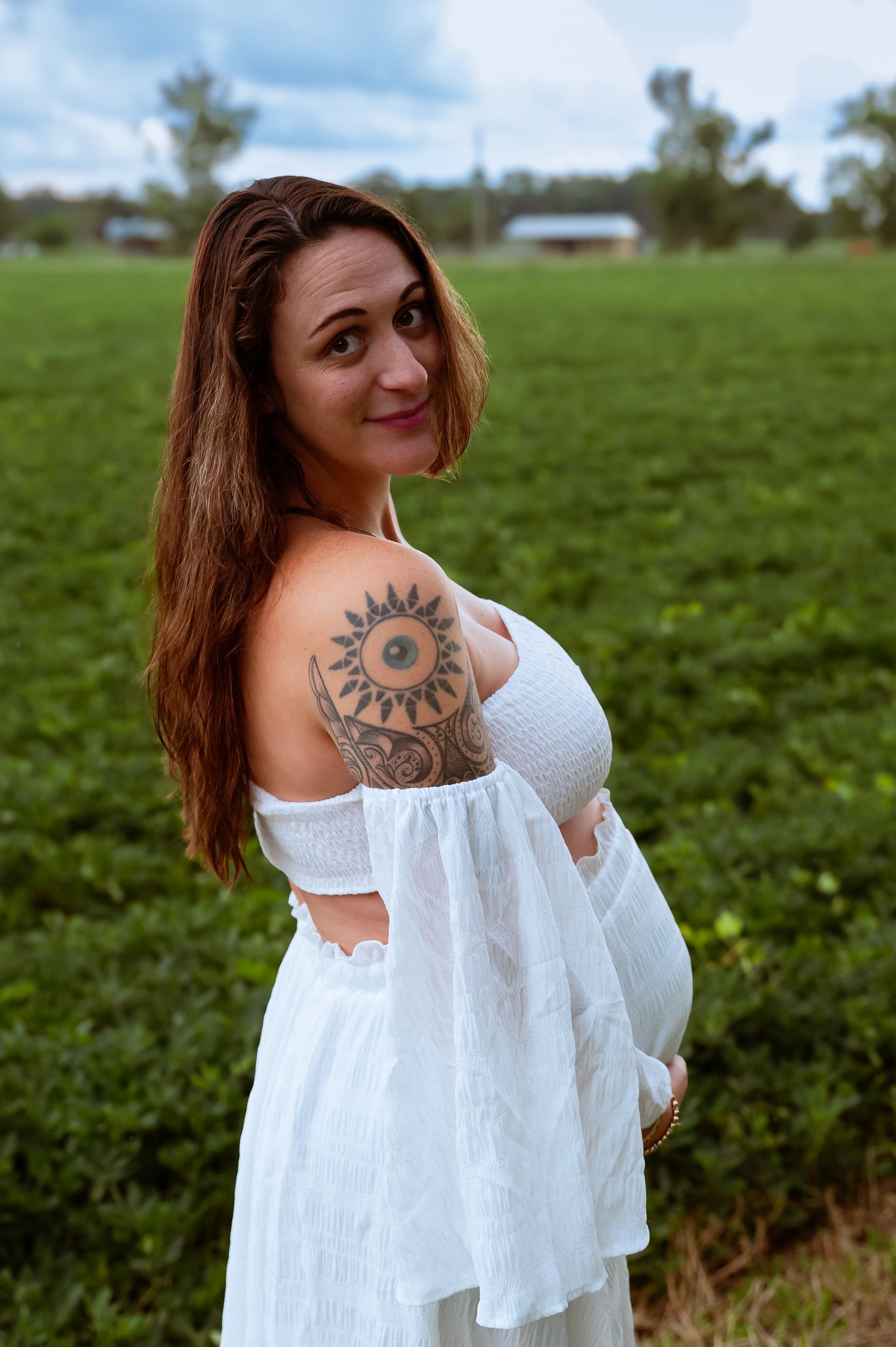 A white off-shoulder dress shown with visible sun tattoo design on shoulder.