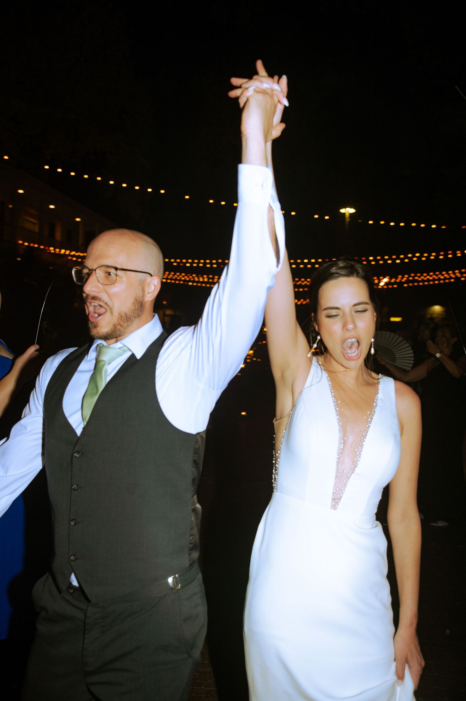 A celebratory dance moment at a wedding reception with string lights in the background.