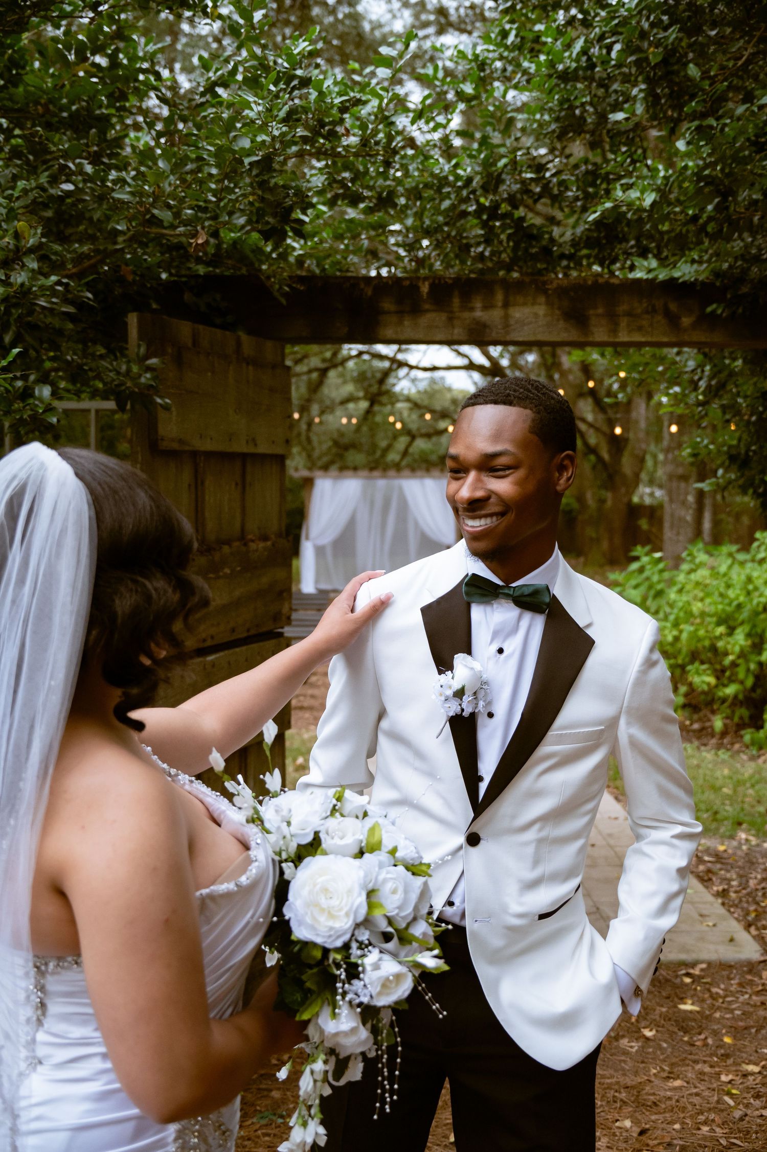 A tender moment between newlyweds in a garden setting with white flowers and formal wedding attire.