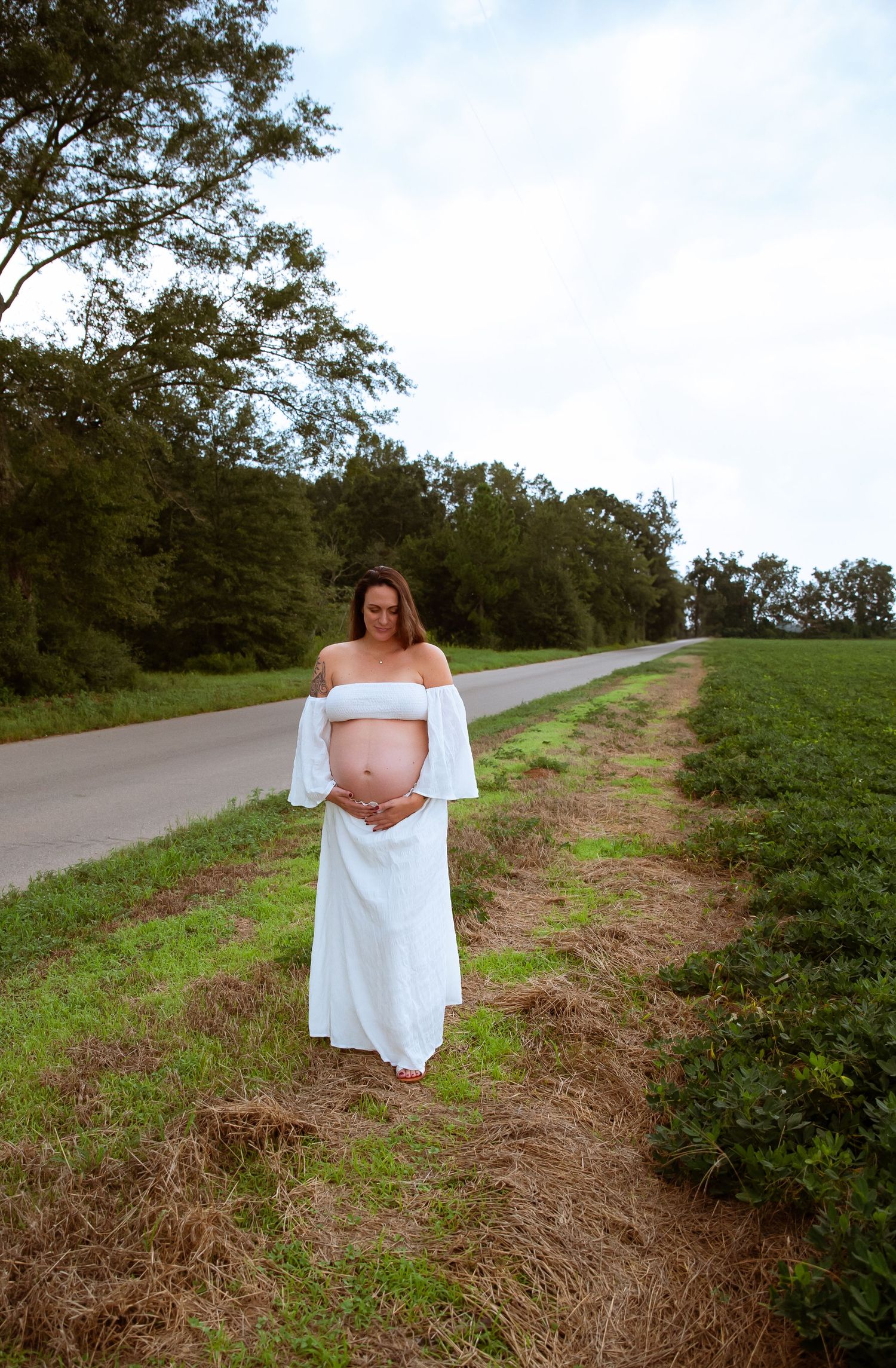 A person in a flowy white dress poses along a countryside path.