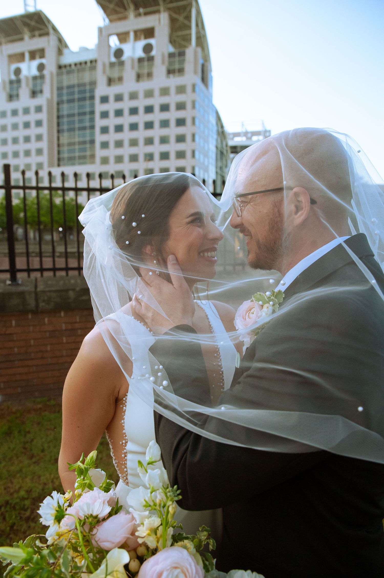 A romantic wedding portrait with a modern city building backdrop.