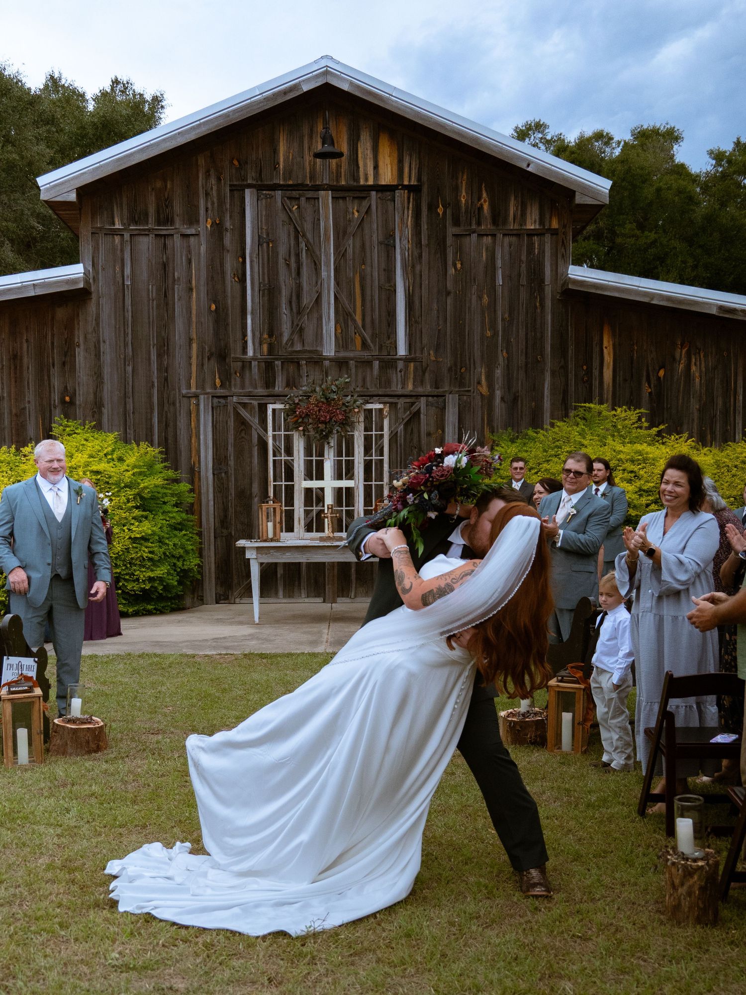 A romantic wedding couple dips in front of a rustic wooden barn venue during a photo session.