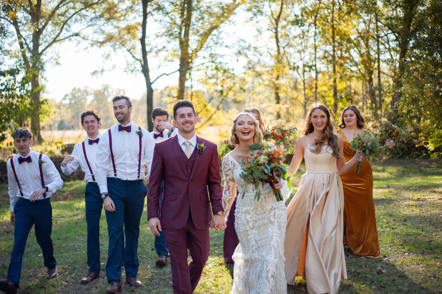 Wedding party in burgundy and navy attire poses together in autumn forest setting during golden hour.