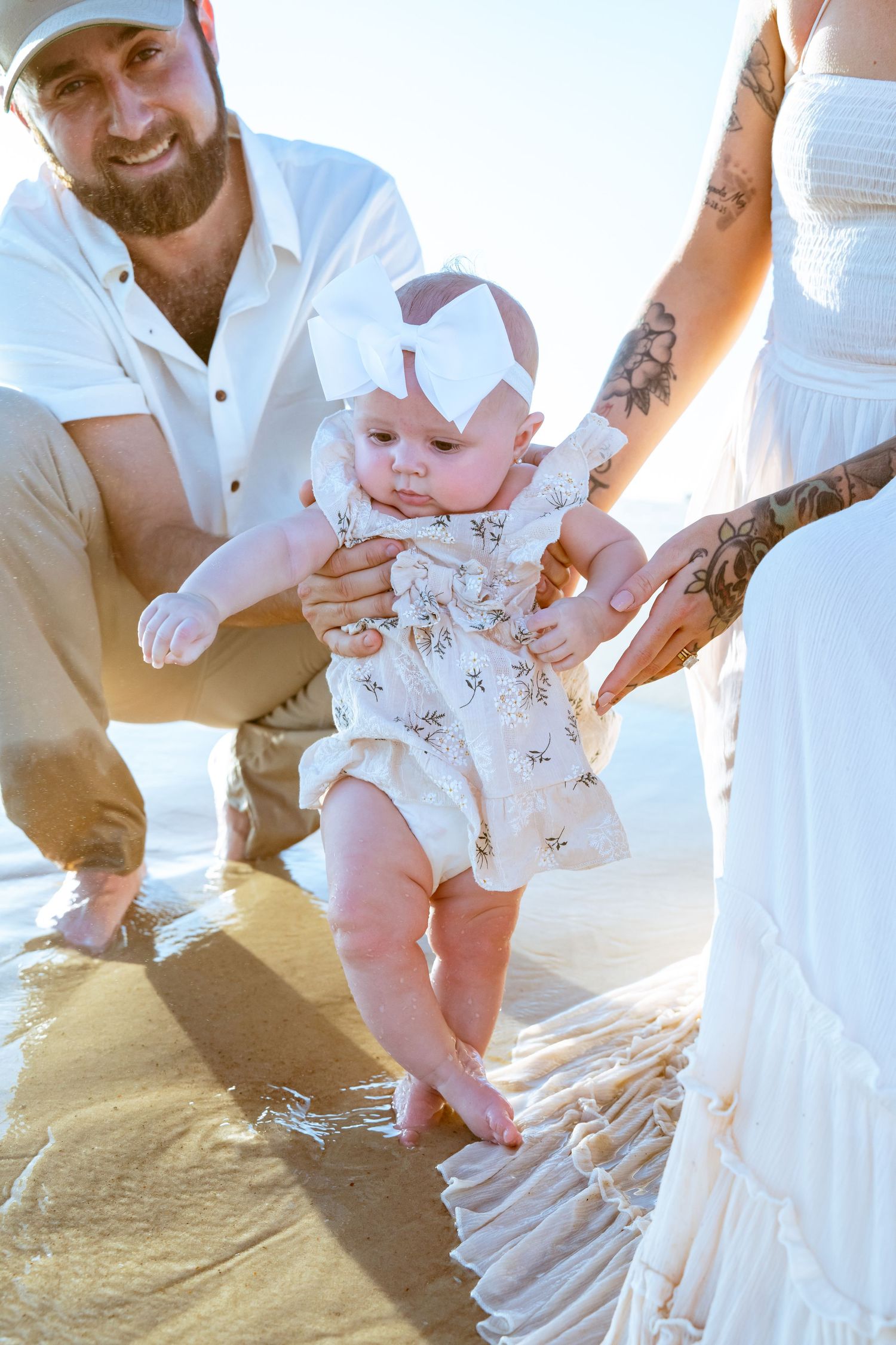 A summer beach photoshoot with a baby in white and floral outfits.