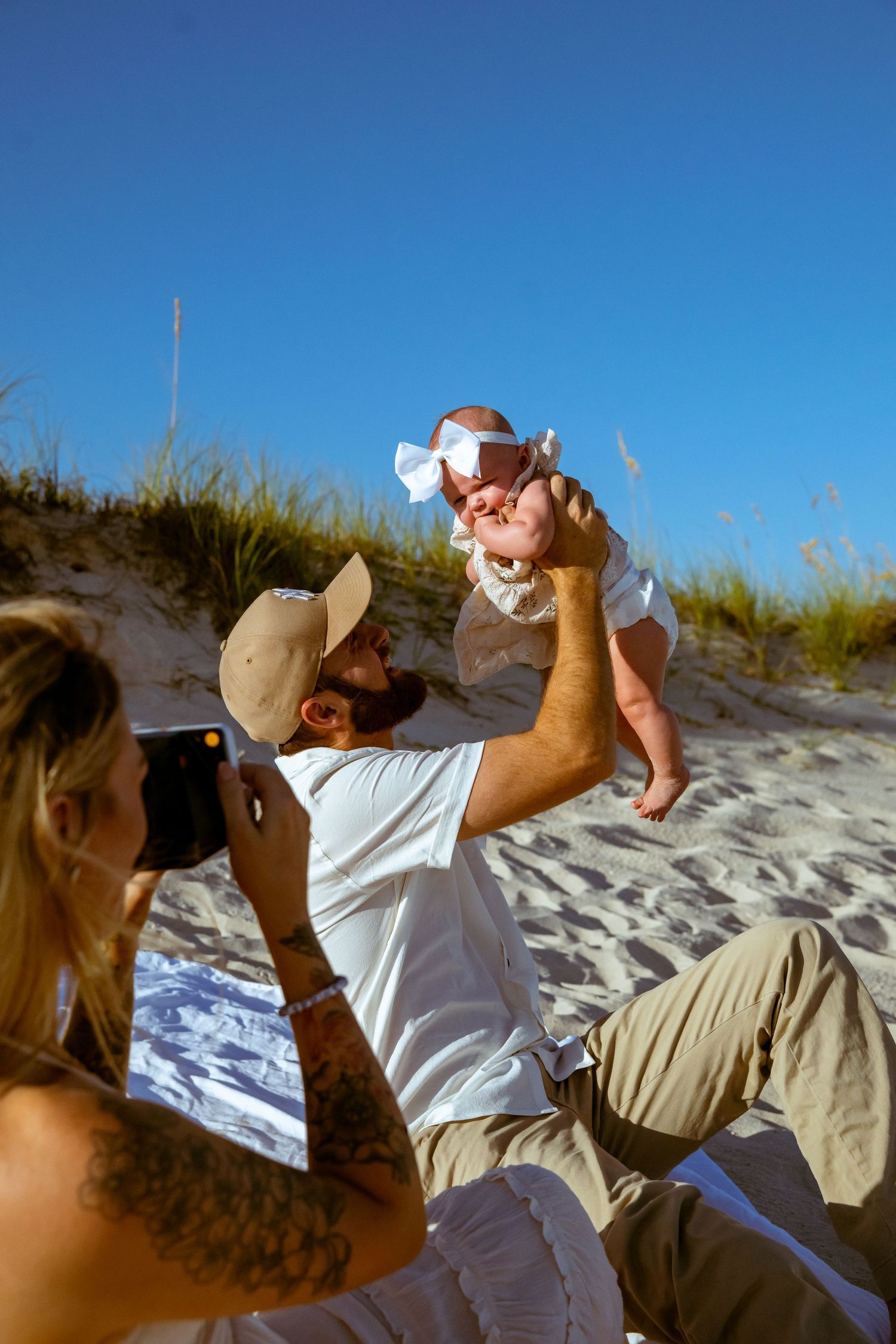A joyful moment captured on sandy dunes with a baby being lifted into blue sky.