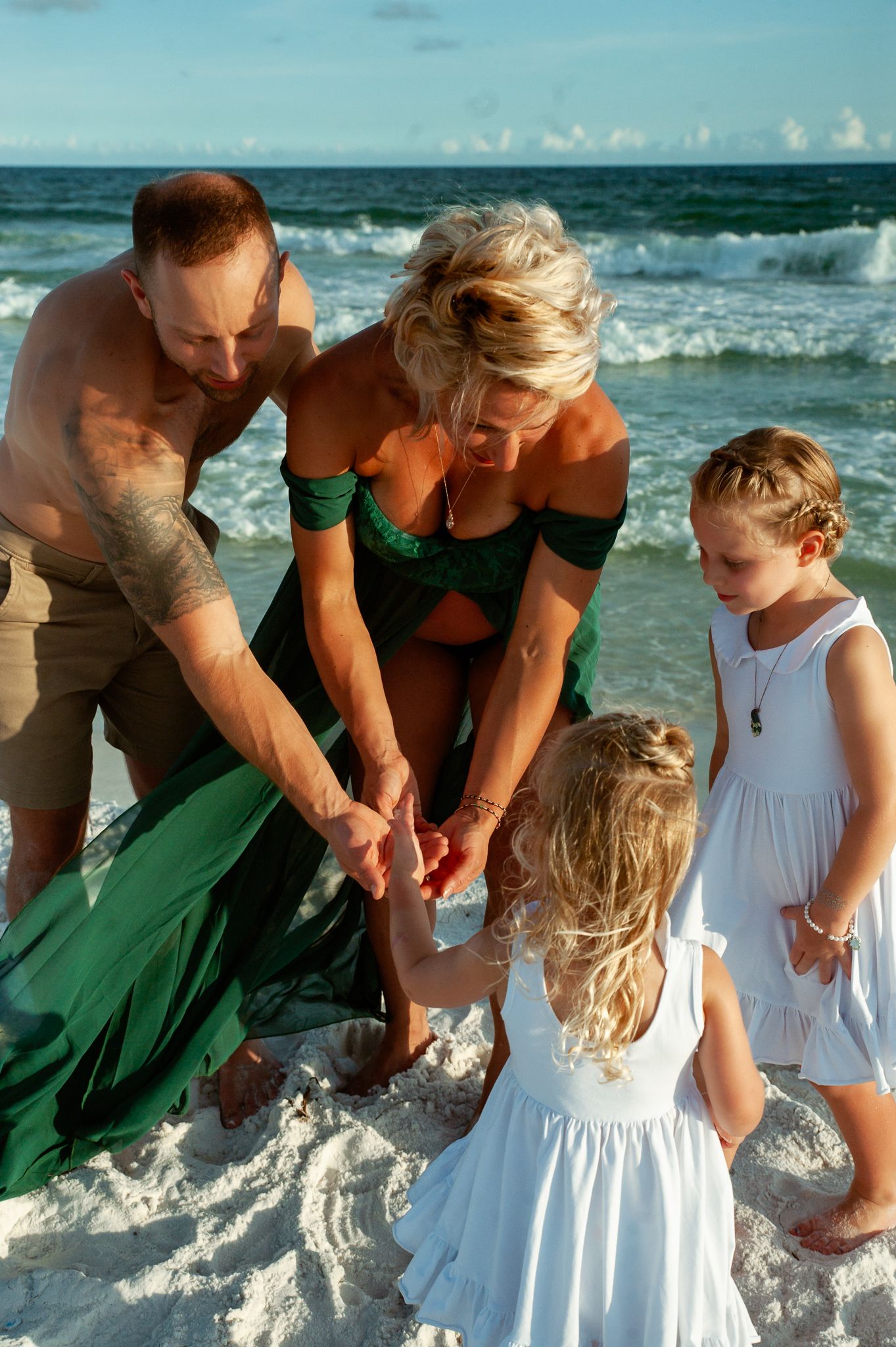 A family gathers on a white sandy beach examining something together while waves roll in behind them.