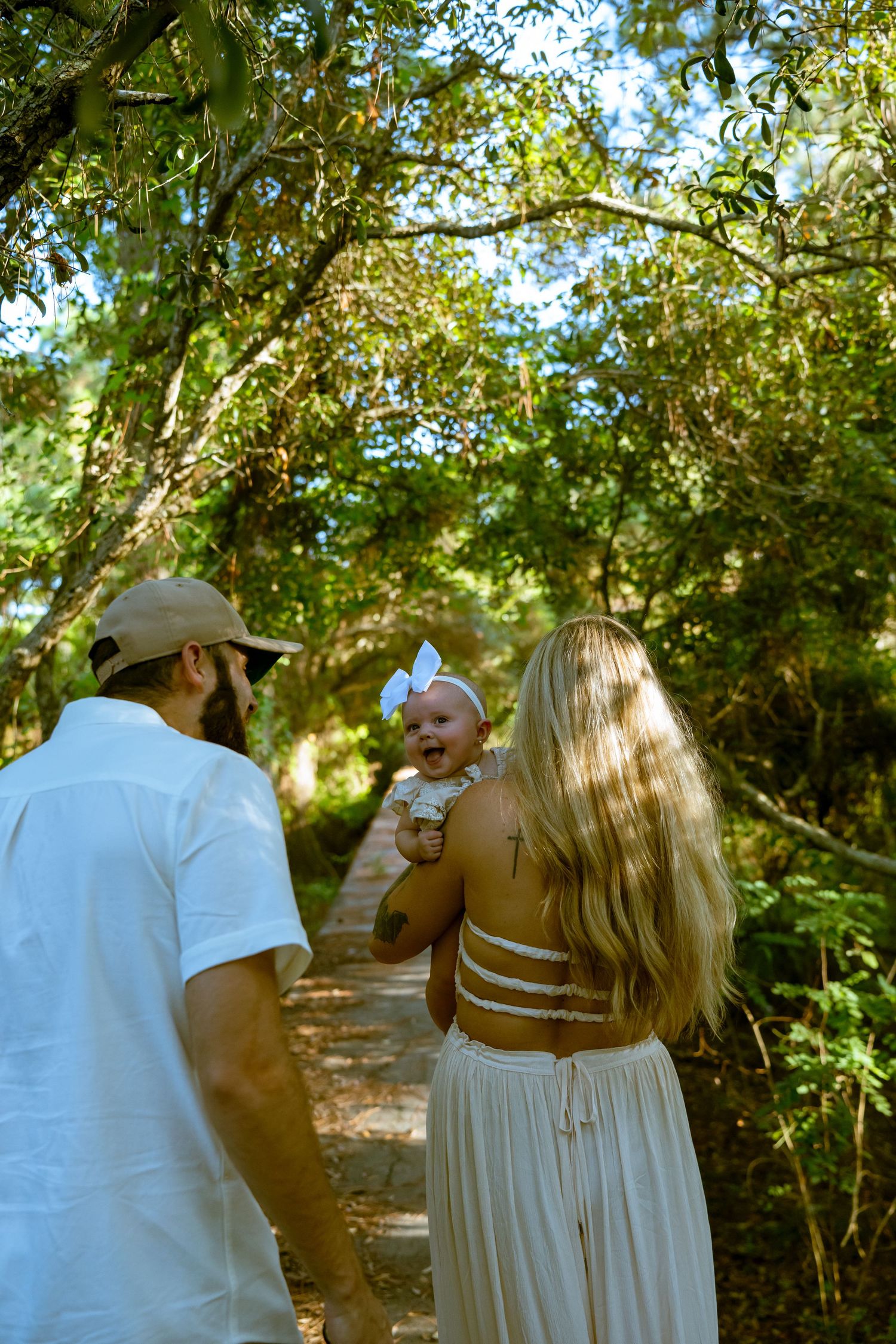 A family walks along a tree-lined nature path on a sunny afternoon.