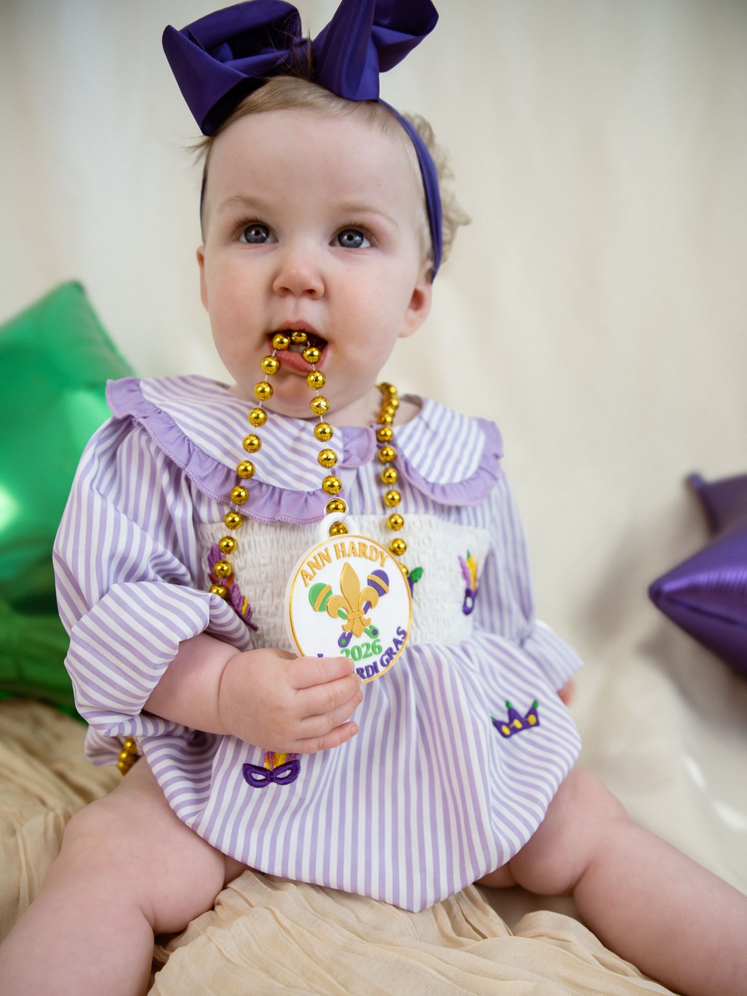 Baby wearing purple bow and striped dress with gold Mardi Gras beads in multiple poses.