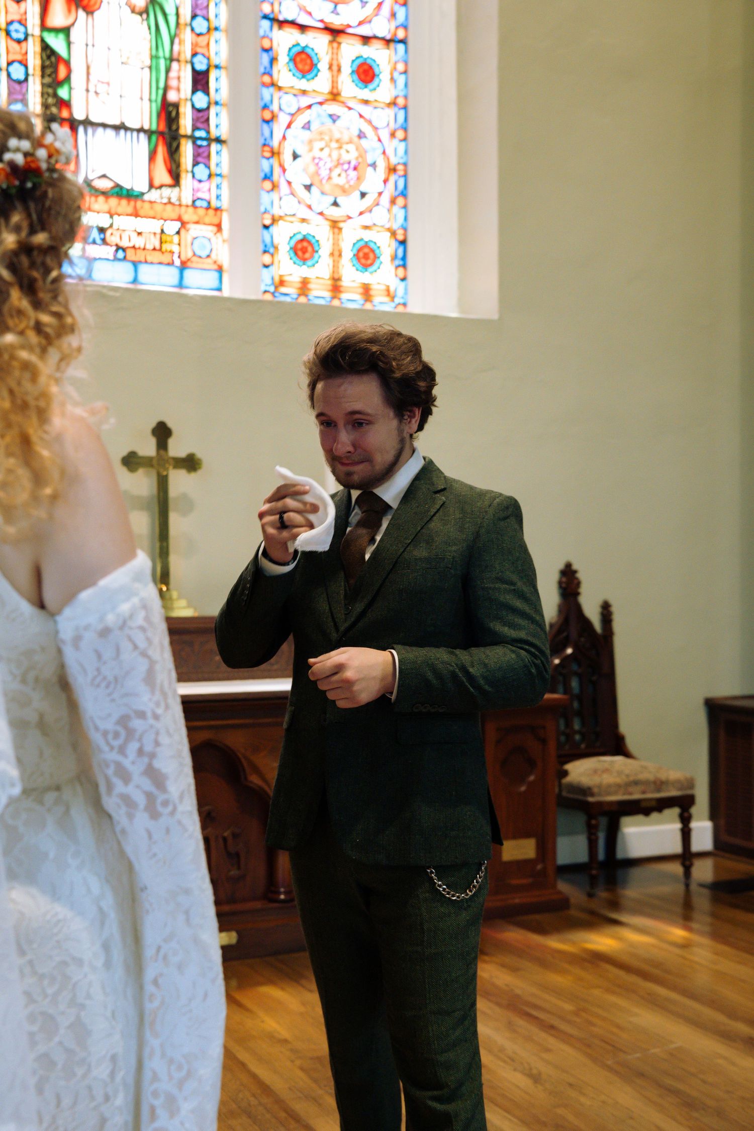 A wedding ceremony in a chapel with beautiful stained glass windows and wooden pews.
