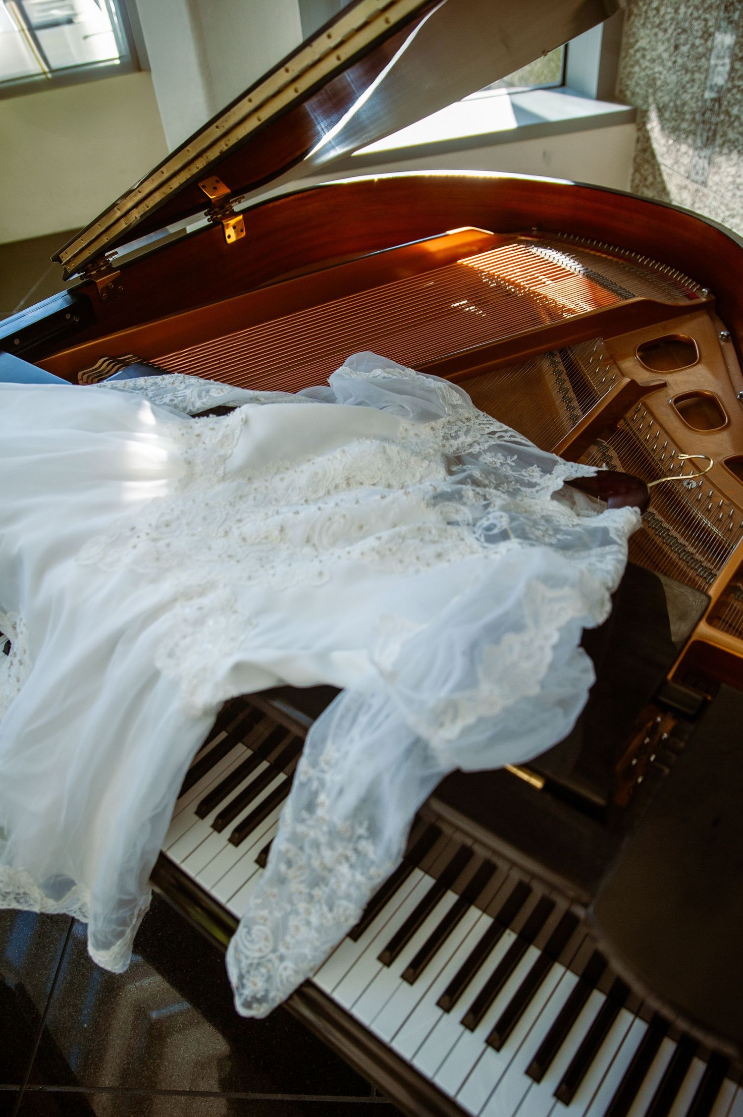Elegant white wedding dress draped across piano keys in dramatic lighting.