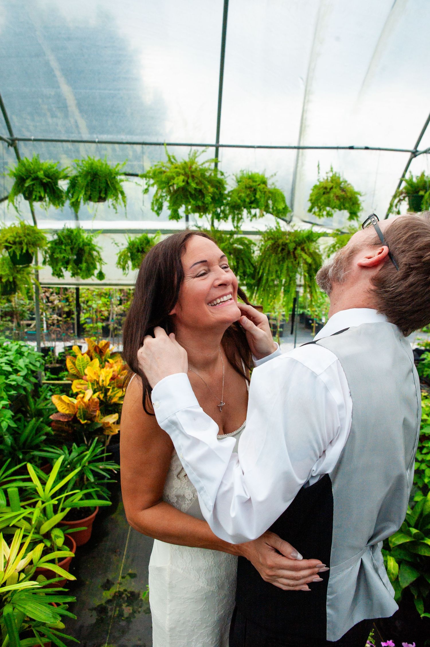 A joyful couple shares laughter in a greenhouse filled with lush greenery and vibrant flowers.