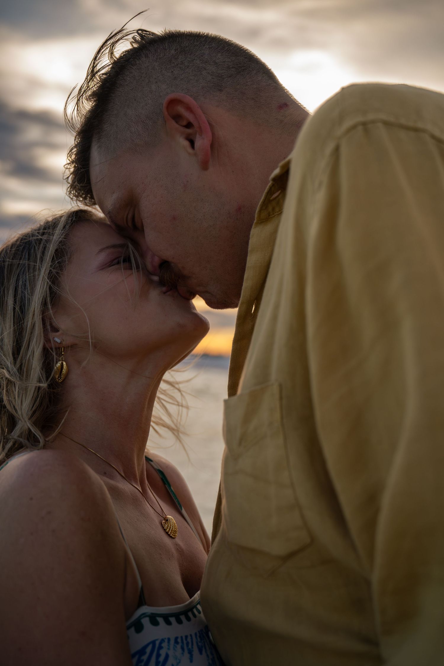 Couple sharing a romantic kiss at sunset on the beach, golden light illuminating their silhouettes.