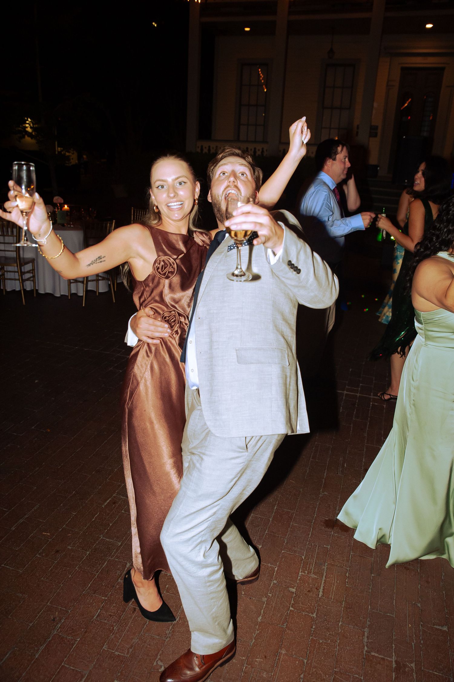 Wedding guests dancing and celebrating at a reception with festive lighting.