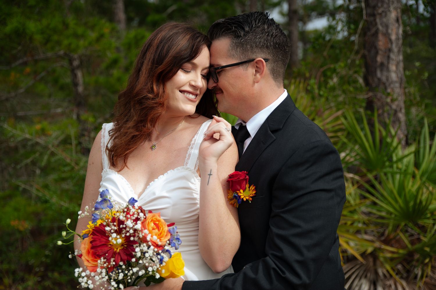 A couple shares an intimate moment in a lush forest setting during their wedding celebration.
