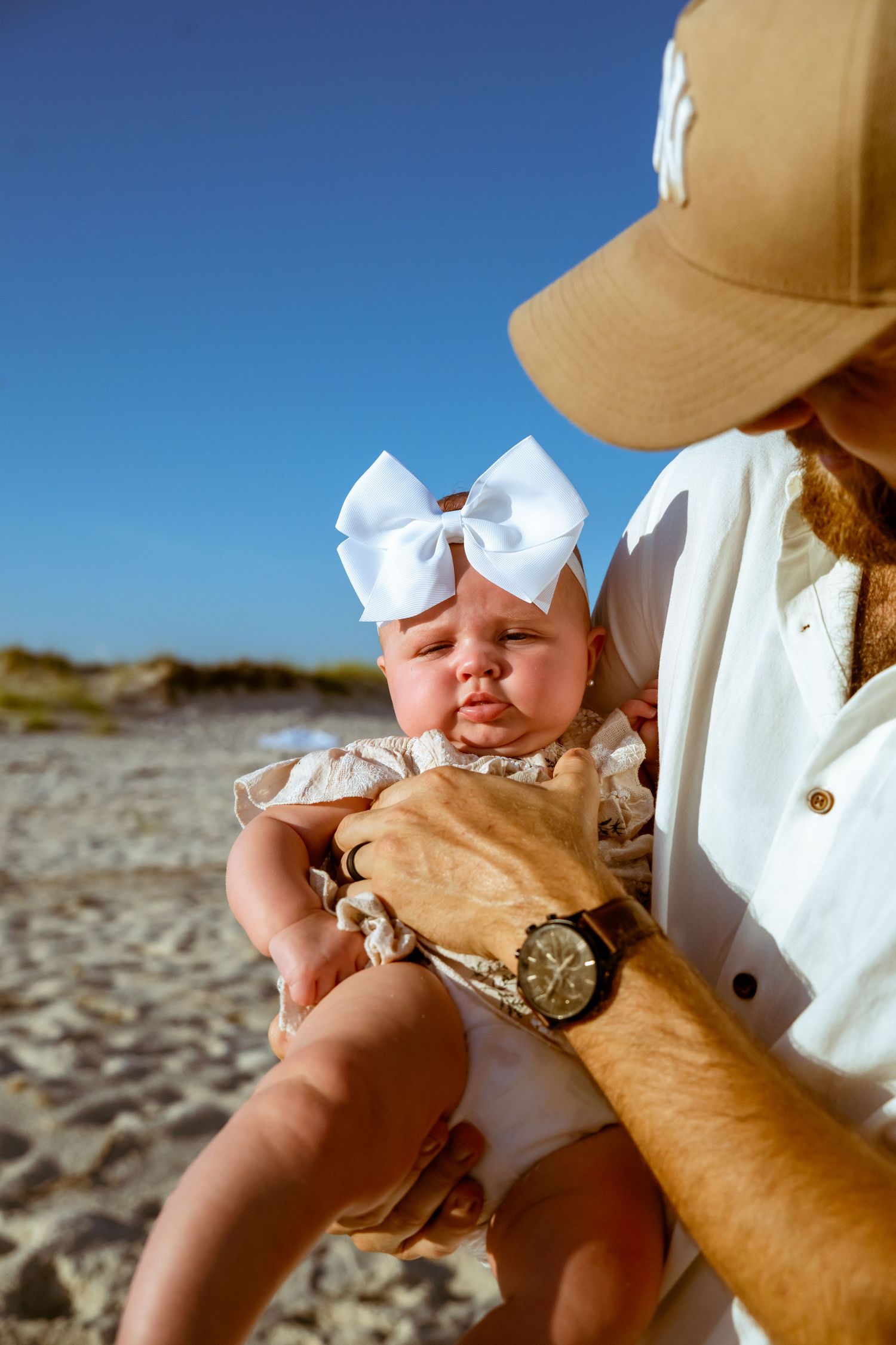 Close-up shots of a baby wearing a white bow on the beach.