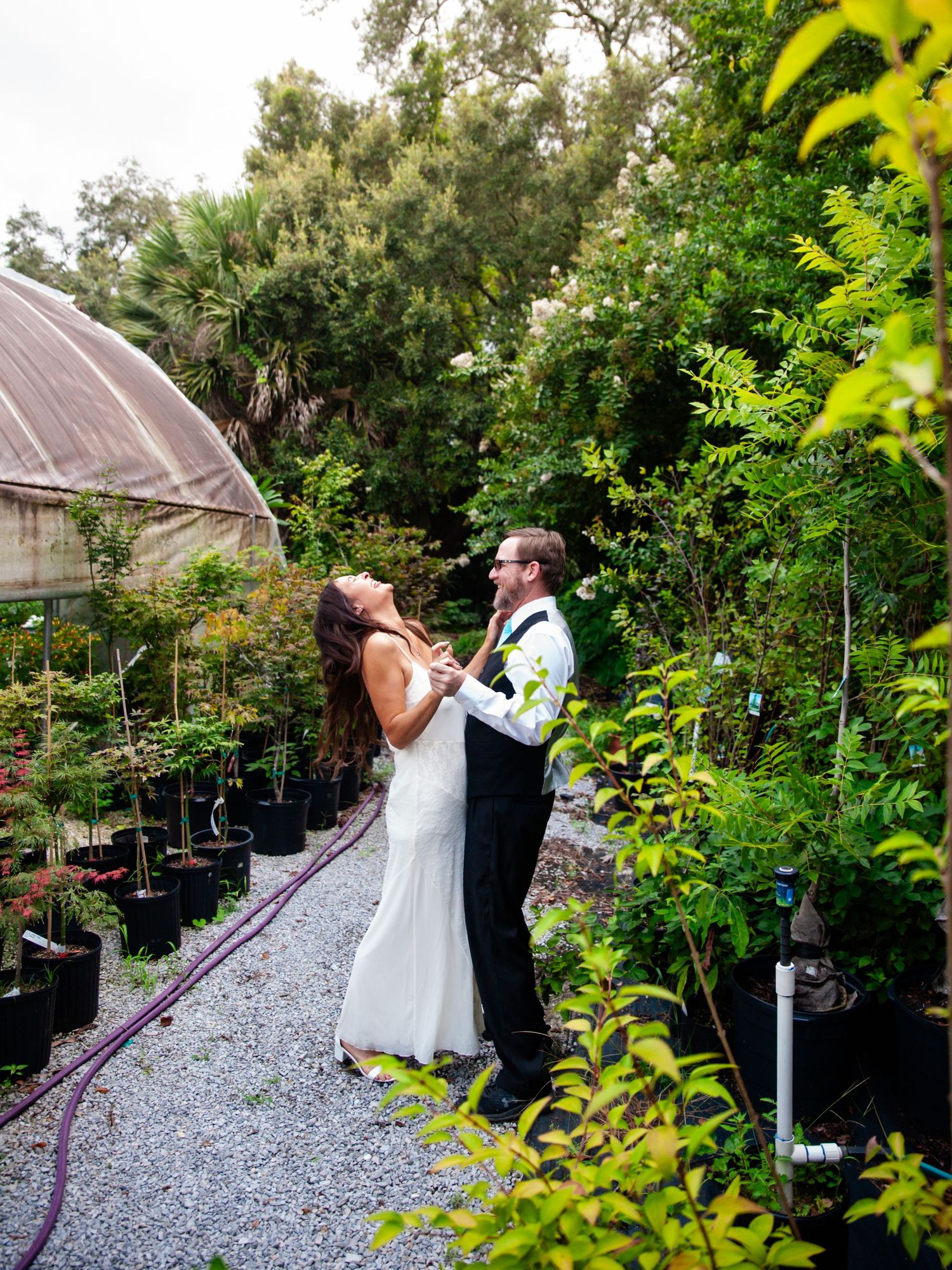 A couple dances amidst lush greenery and gravel paths in a scenic outdoor setting.