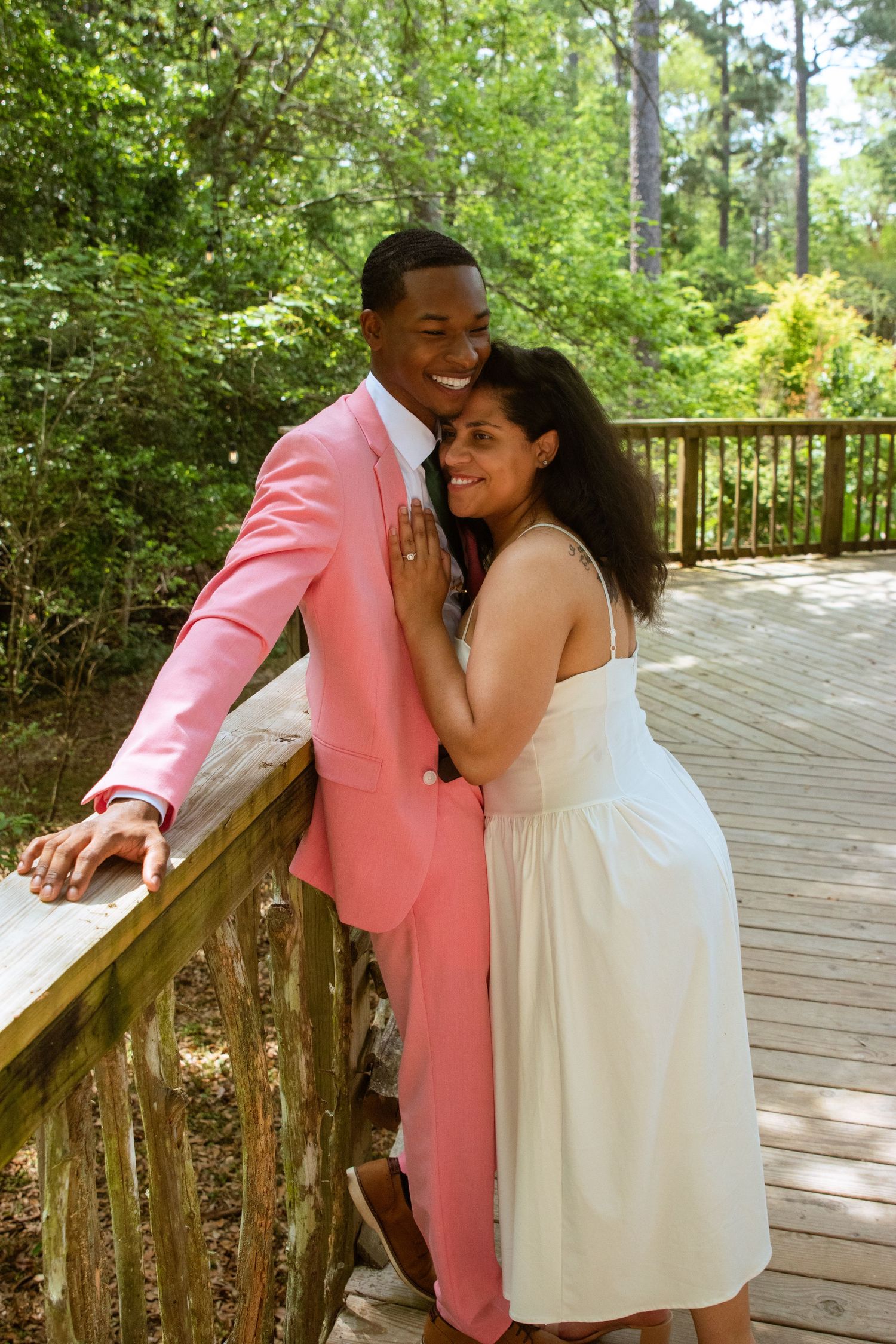 A couple poses together on a wooden deck surrounded by lush greenery.
