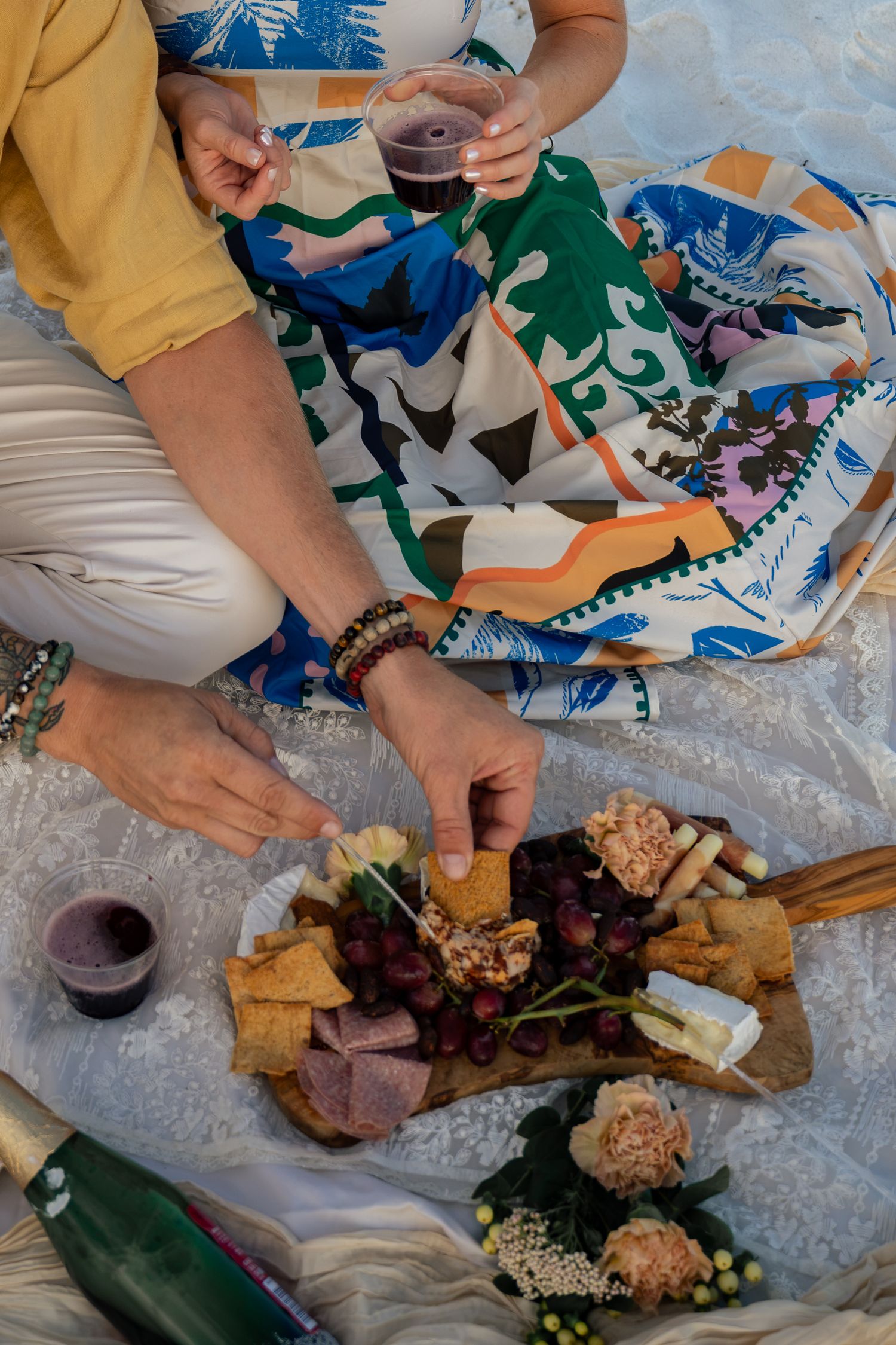 Person enjoying a charcuterie board with grapes, crackers, and cheese at a picnic with red wine.