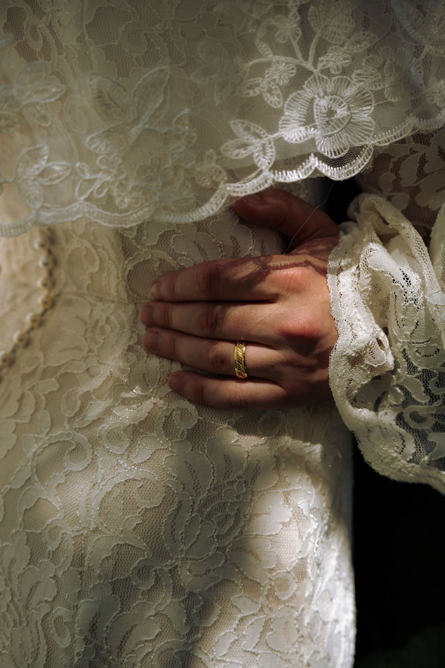 A detailed close-up of hands touching delicate lace wedding dress fabric.