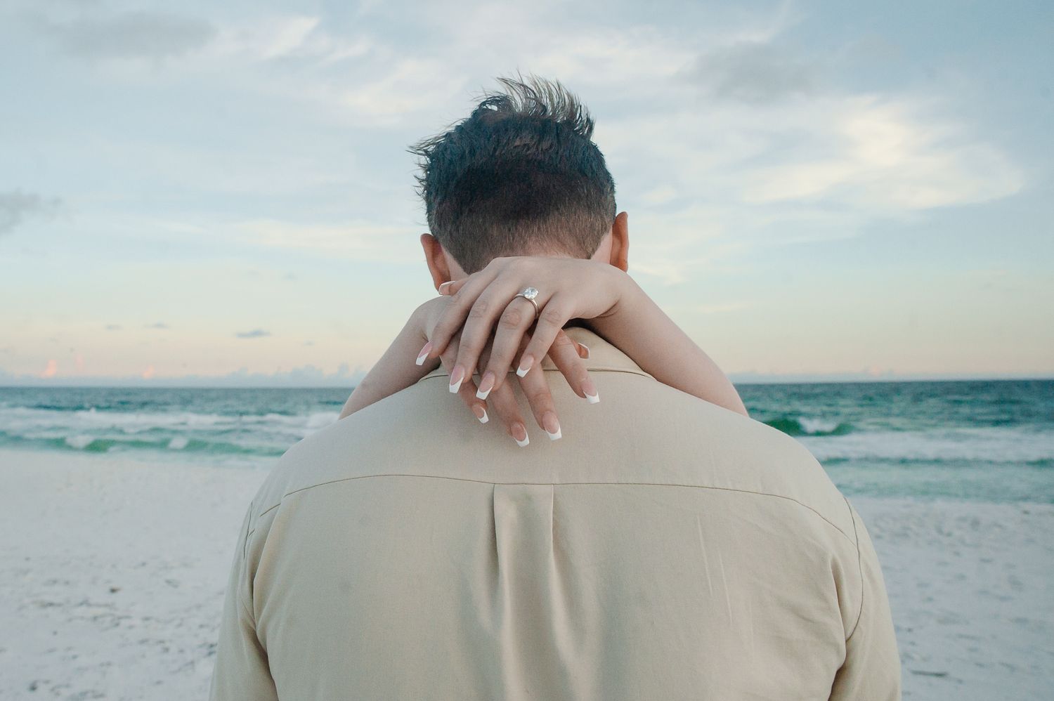 A couple walks hand in hand on a white sandy beach at sunset with gentle waves crashing in the background.