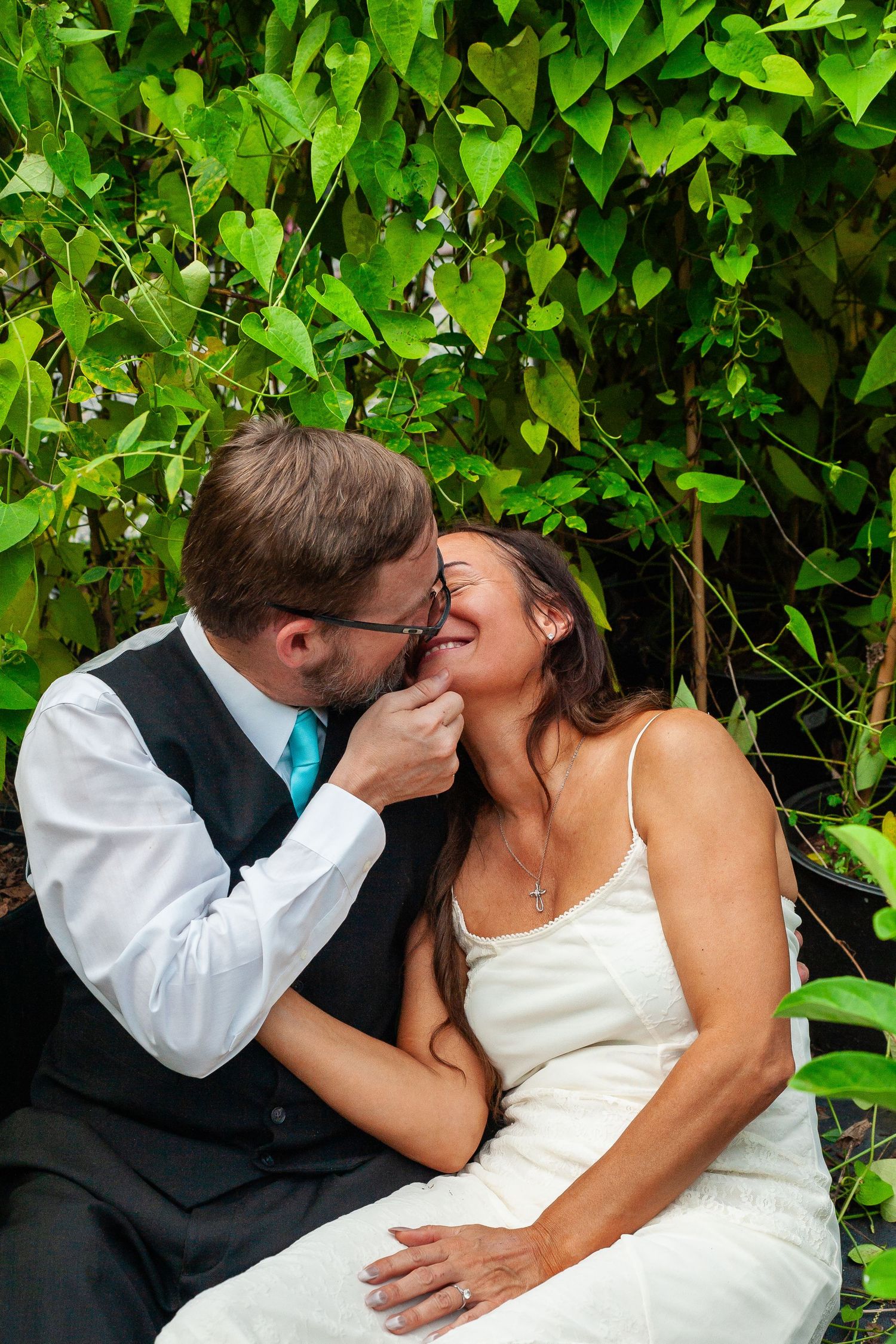 Newly married couple sharing multiple romantic kisses against a backdrop of lush green foliage in the garden.