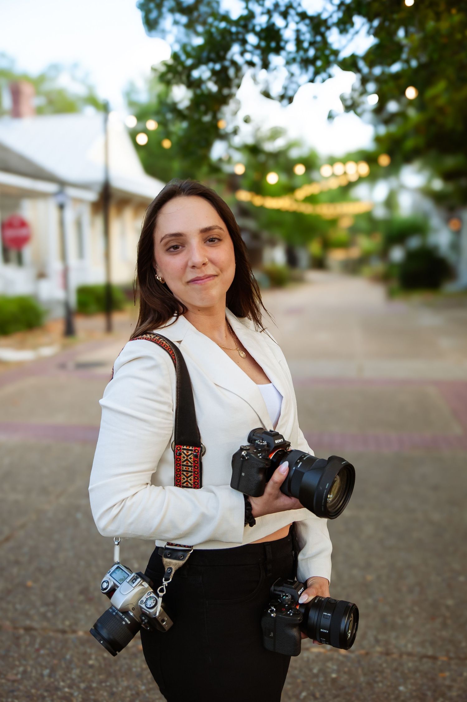 Professional photographer in white jacket poses with camera gear on city street.