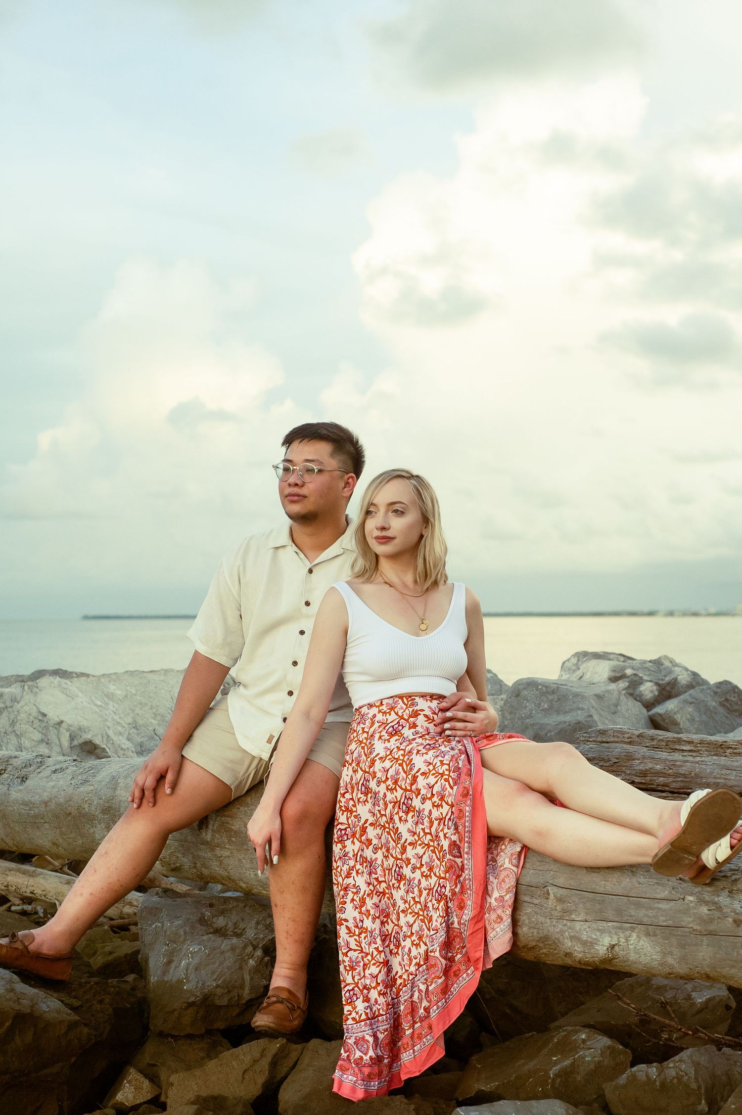 Two people relaxing on coastal rocks with ocean waves in background.