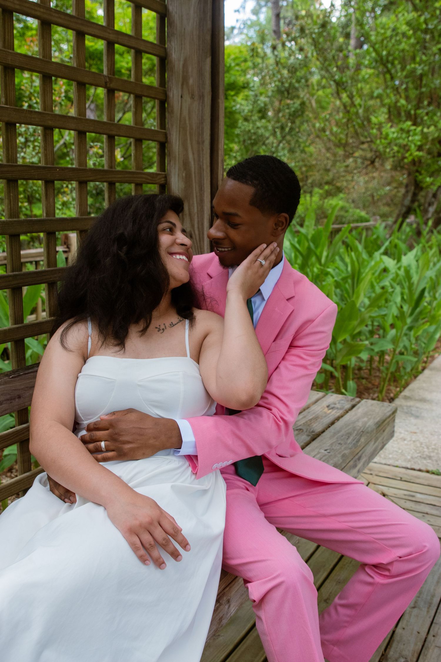 A couple shares an intimate moment on a wooden bench in their wedding attire.