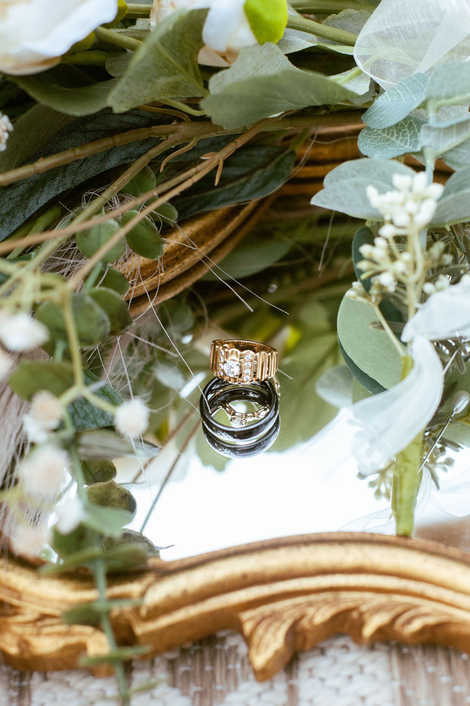 Wedding rings artistically arranged among green leaves and white flowers.