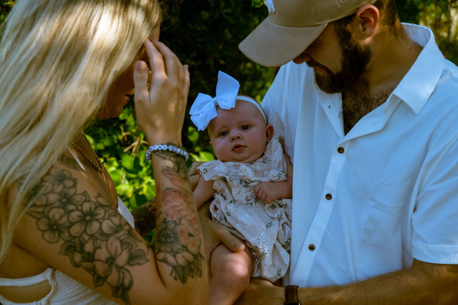 An intimate family moment captured outdoors with a small infant wearing a white bow.