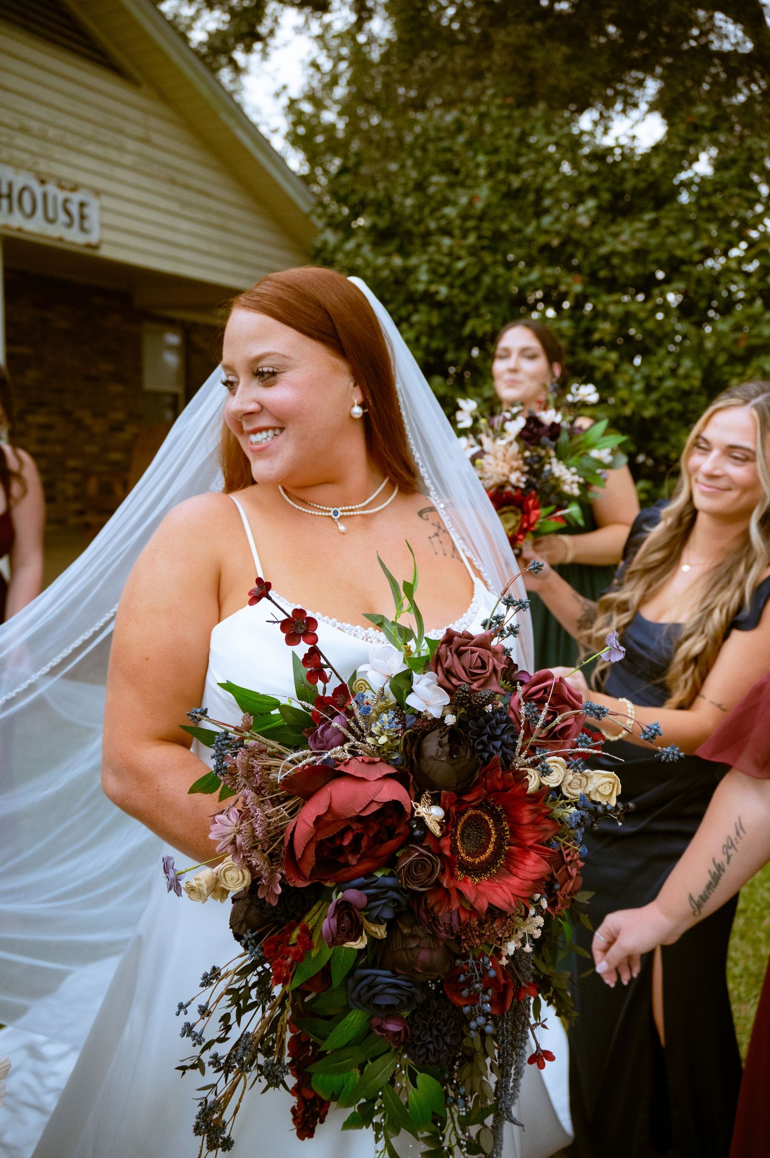 A wedding bouquet features deep burgundy roses, white flowers and dark foliage against a white dress.