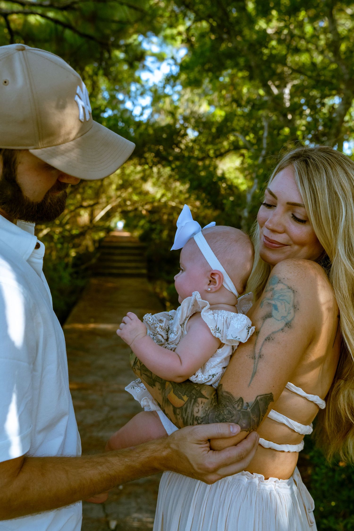 A loving family moment captured on a wooded path with a small baby wearing a white bow.