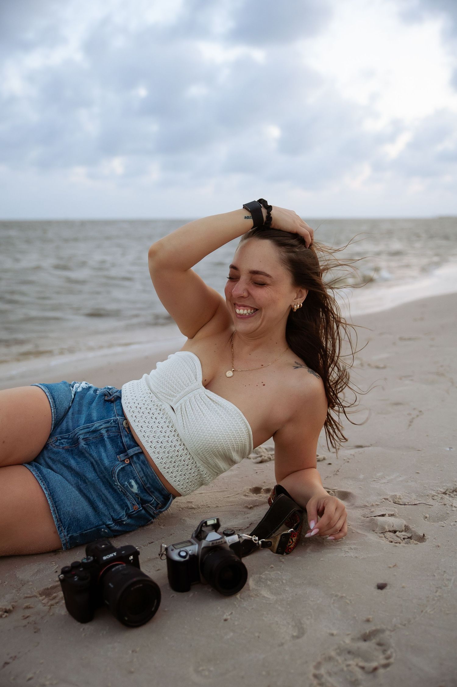 Casual beach portrait session with white crochet top and denim shorts on sandy shore.