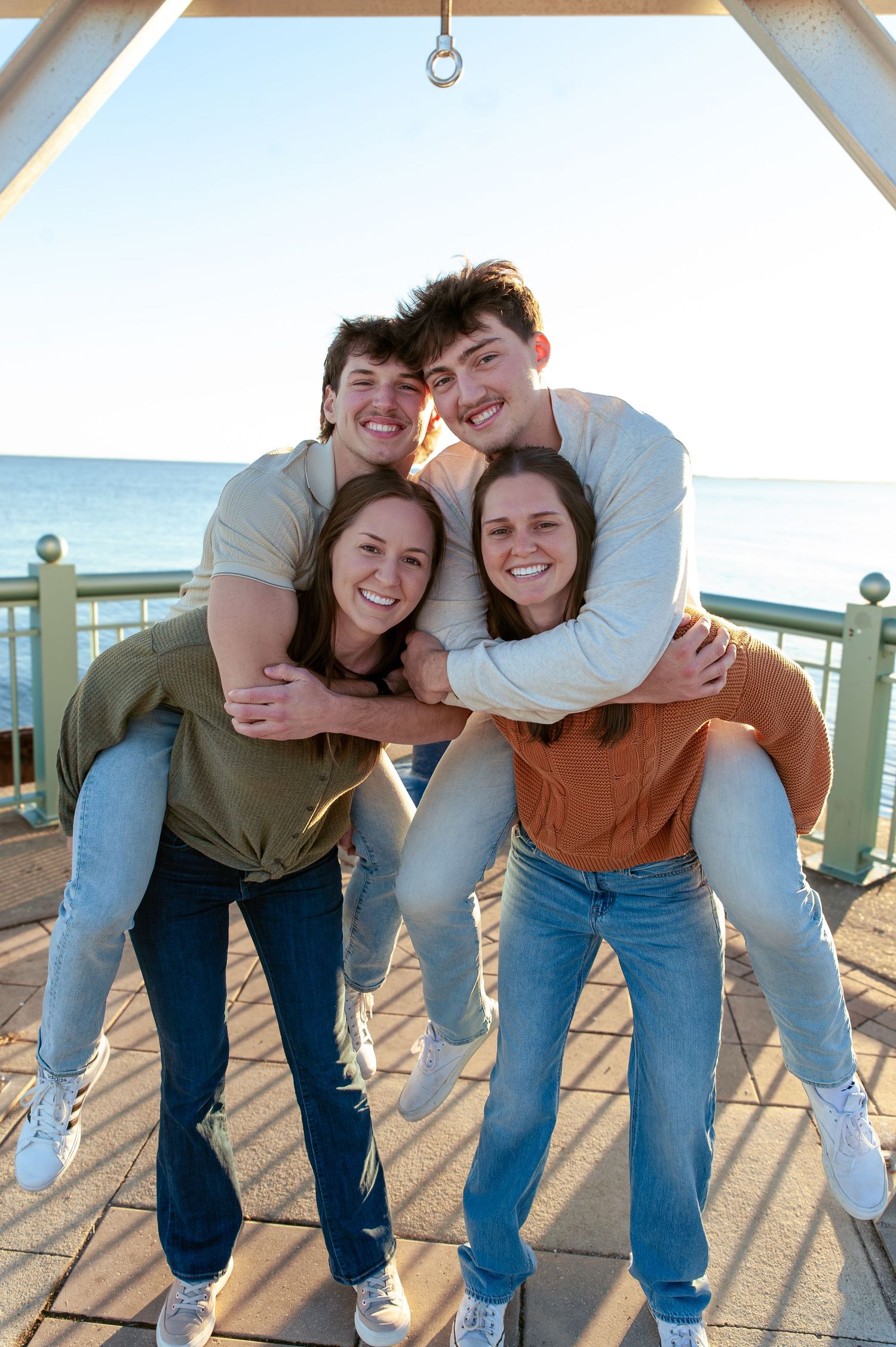 A group of friends pose playfully together on a wooden deck at sunset.