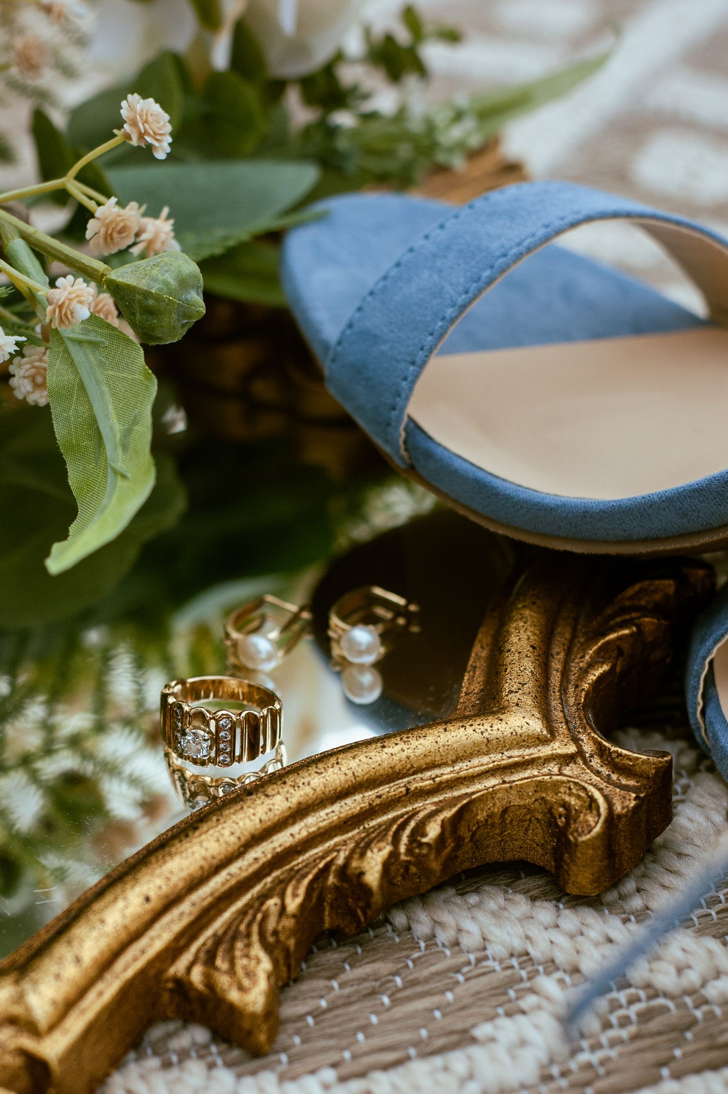 Blue wedding shoes and gold rings displayed with delicate floral accents.