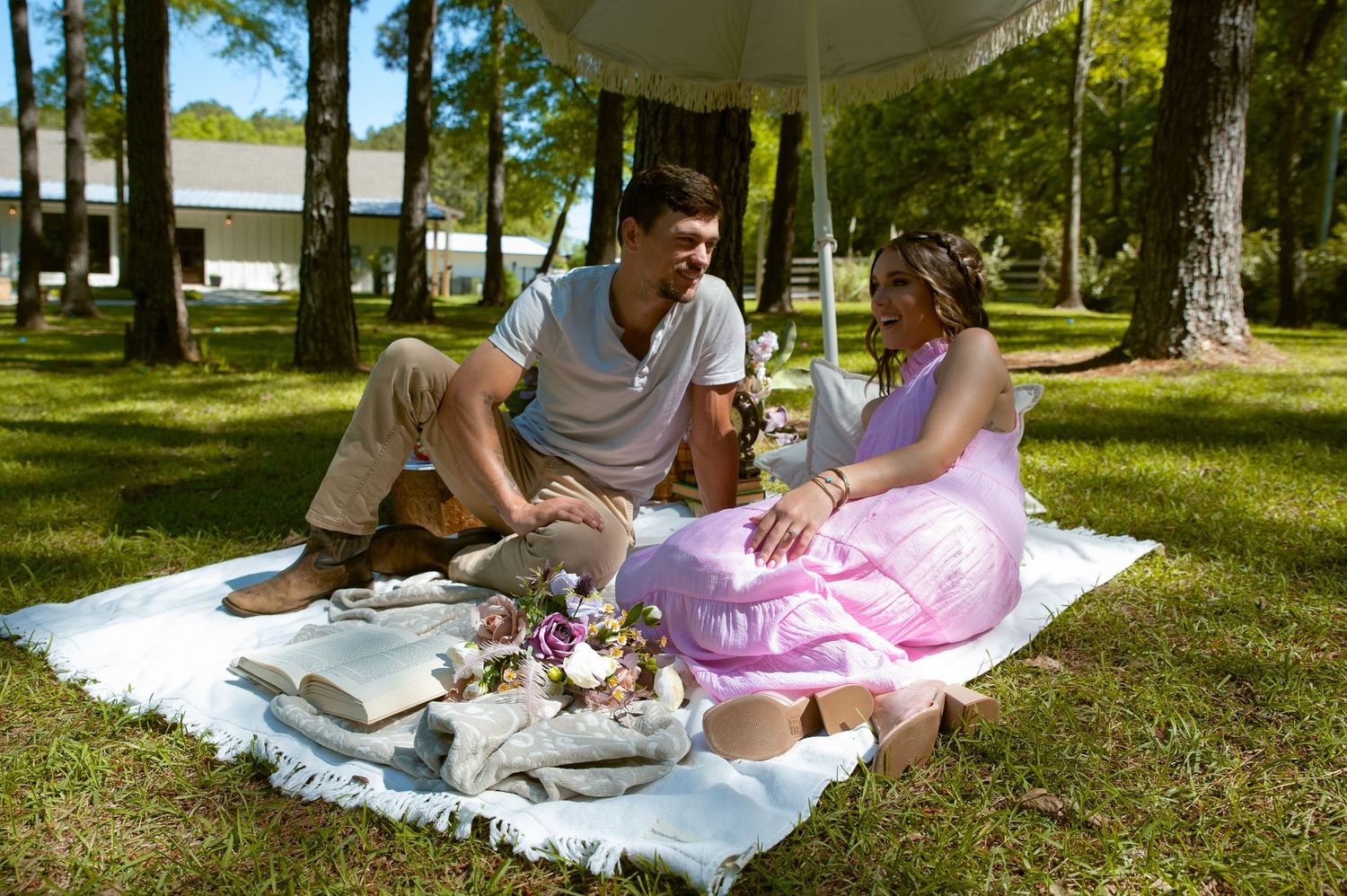 Couple having a romantic picnic on a white blanket under trees in a sunny park.
