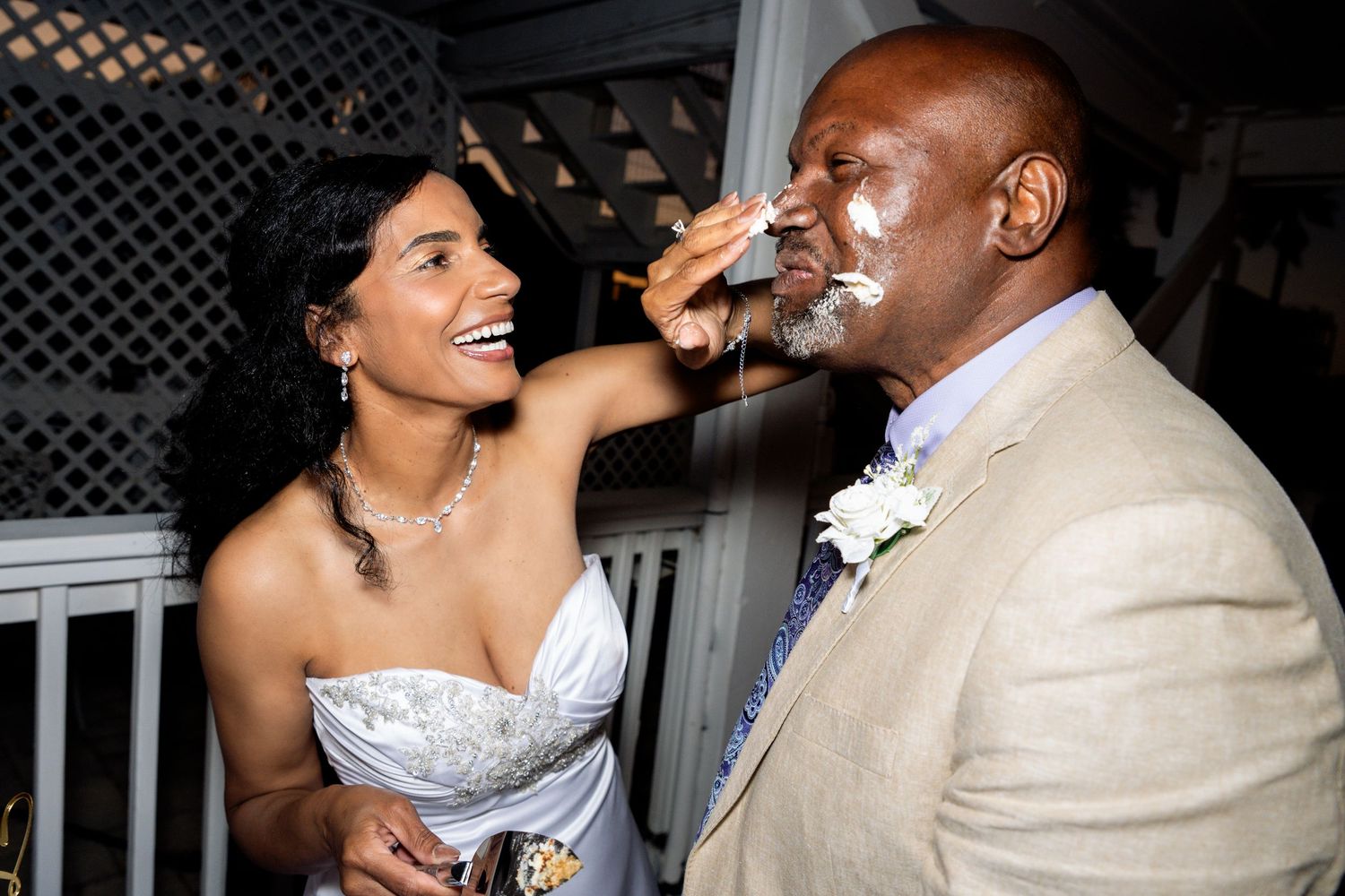 Bride playfully smearing wedding cake on groom's face during reception celebration.