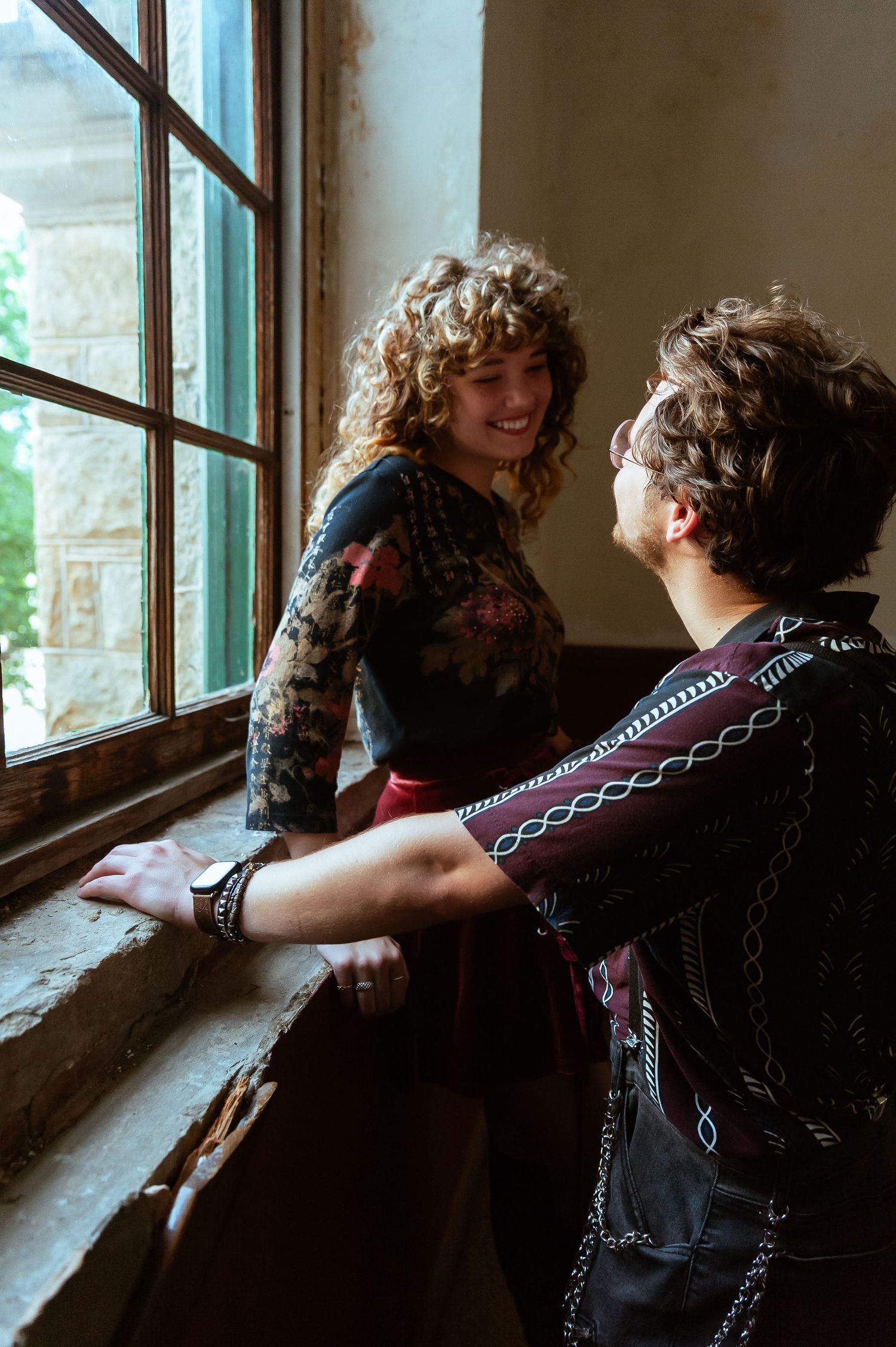 A couple shares quiet moments by a window in a rustic interior setting.