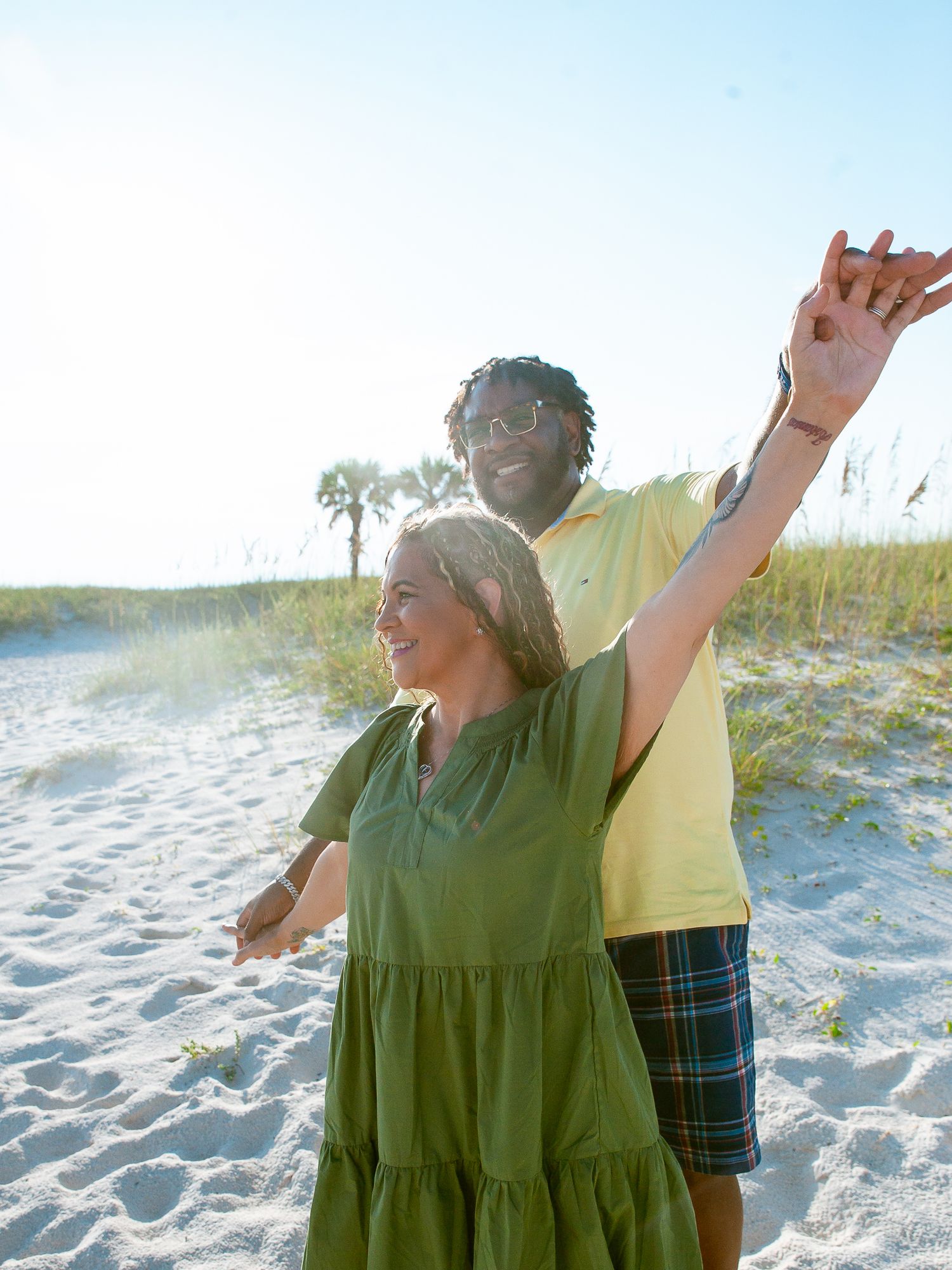Senior couple enjoying a sunny day walking and playing on a white sandy beach with dune grass in the background.