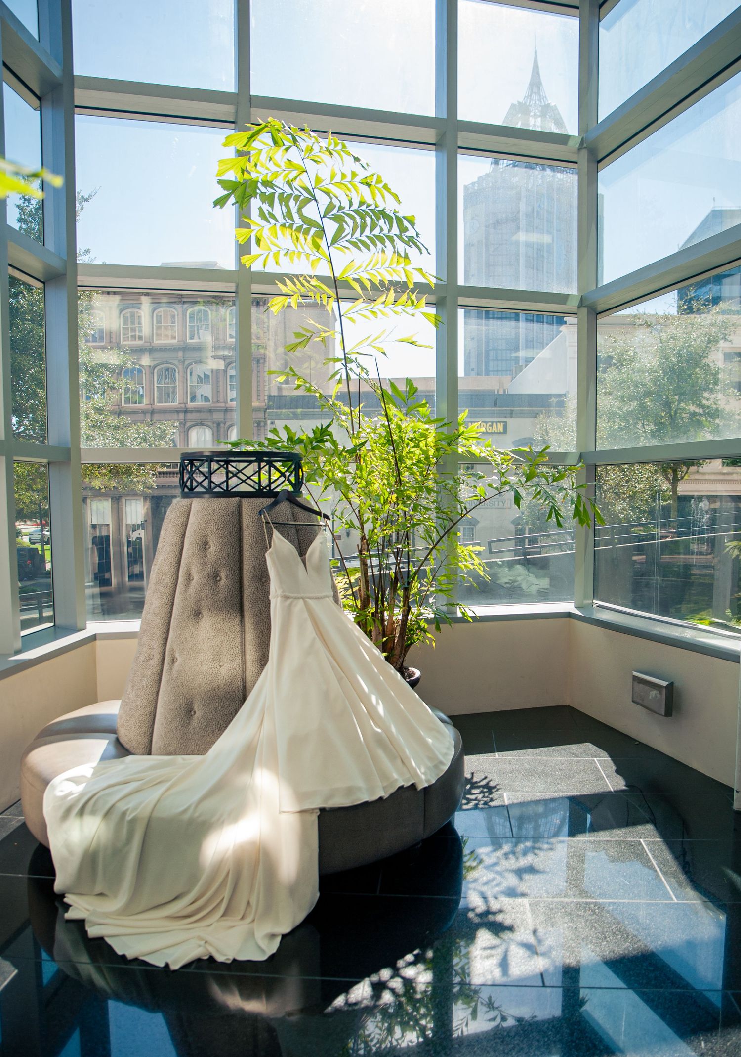 White formal dress displayed in a sunlit room with large windows and indoor plants.