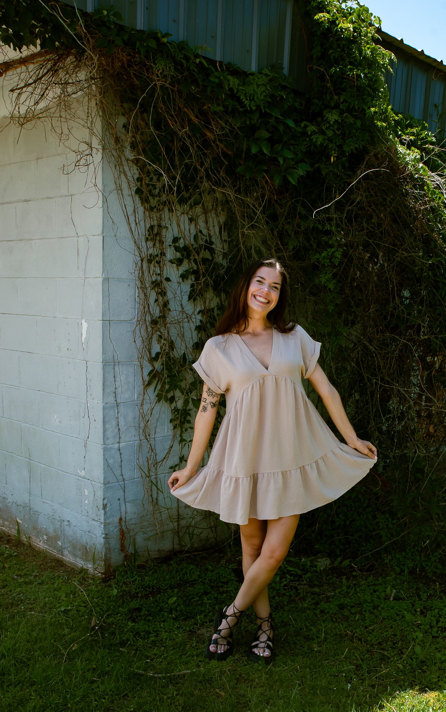 Playful poses in flowing beige dress against white wall with ivy.