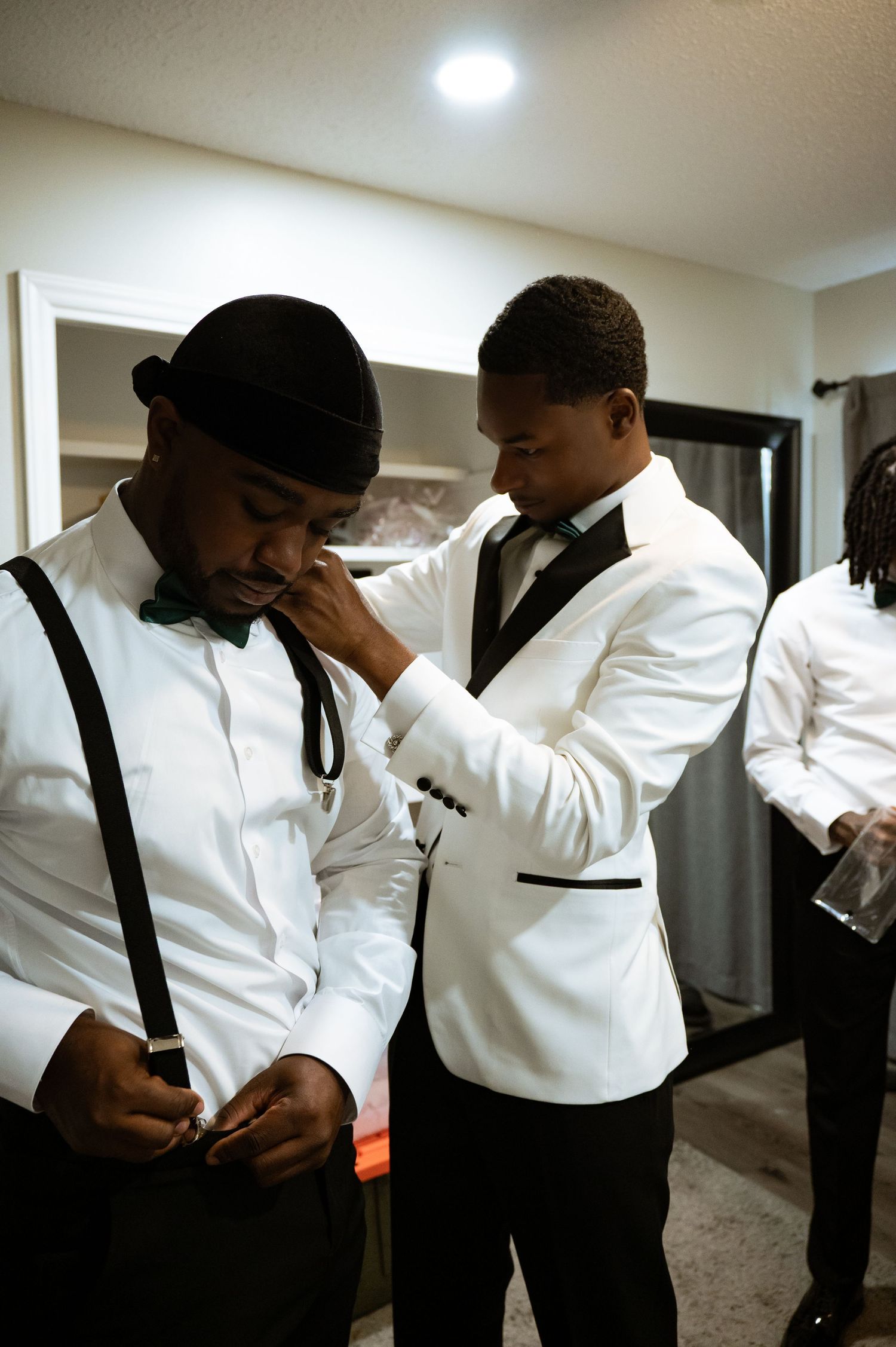 A group in formal white dress shirts and black suspenders prepare for an event in a hallway.