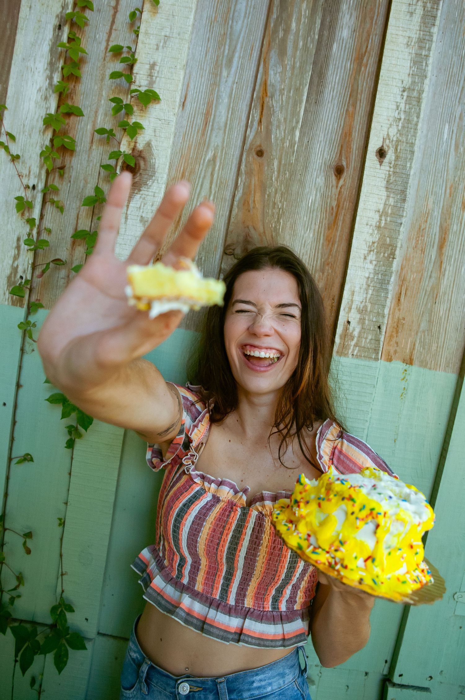 Person in striped top excitedly tosses bright yellow donut against wooden fence.