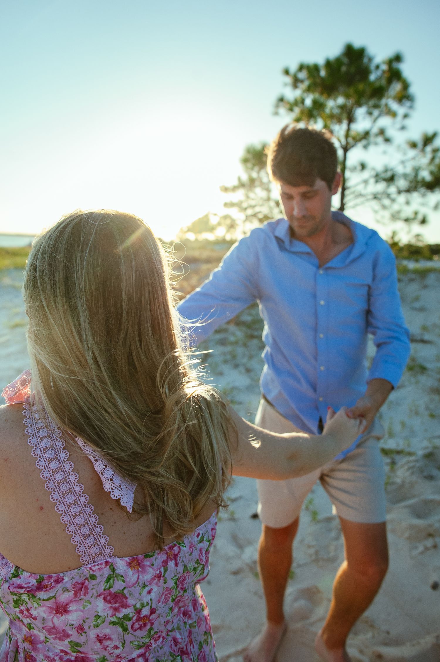 A candid beach scene at sunset showing a light blue shirt and floral dress in the foreground.