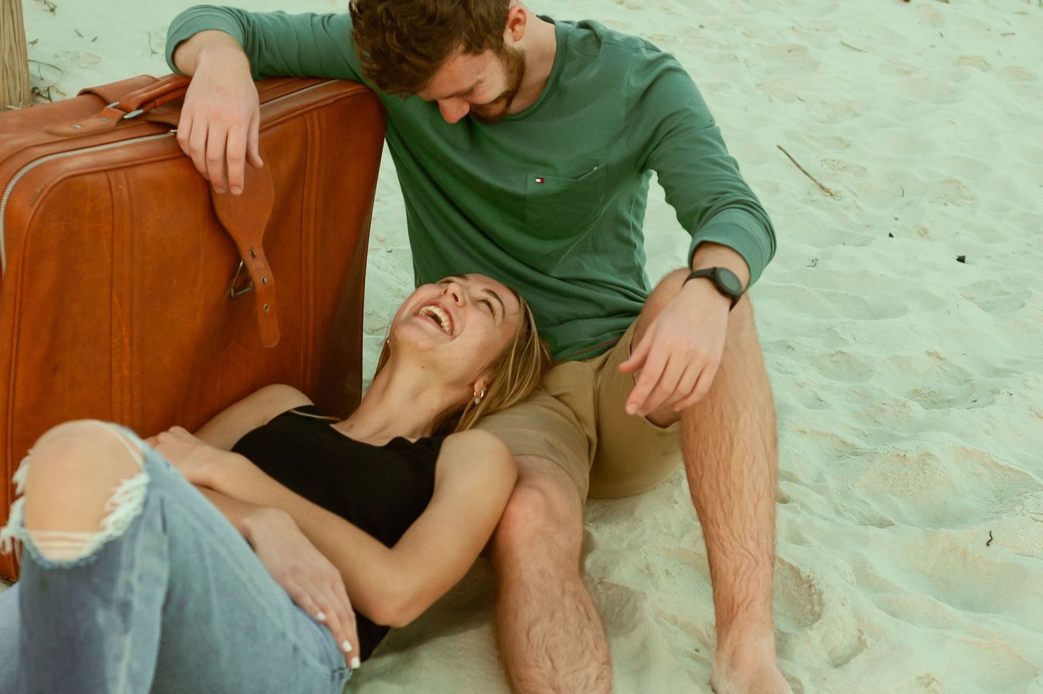 Joyful moment shared on a beach with vintage suitcase and casual attire.