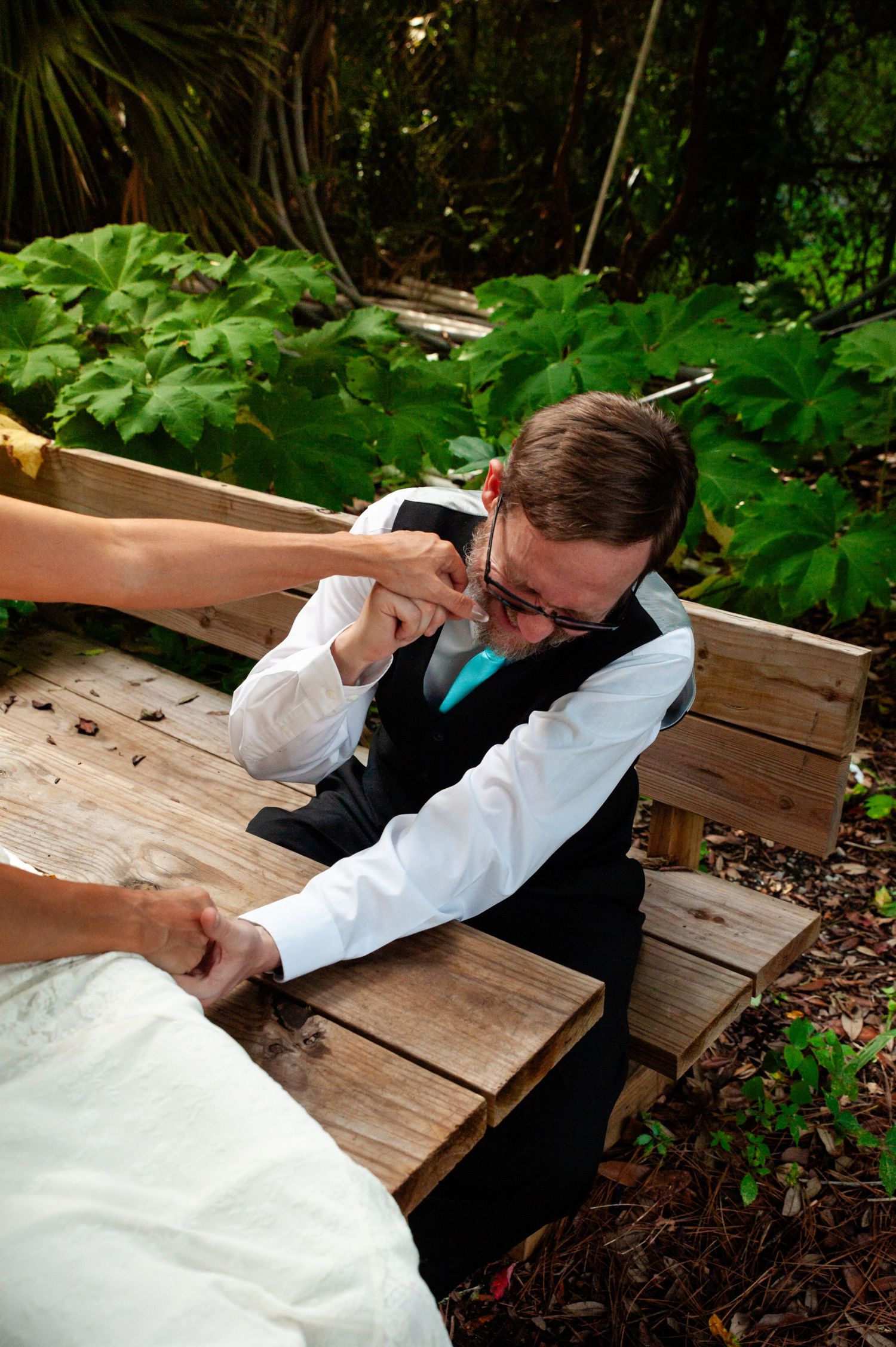A person in formal attire lies on a wooden deck in a lush garden setting, making a photo series in various poses.