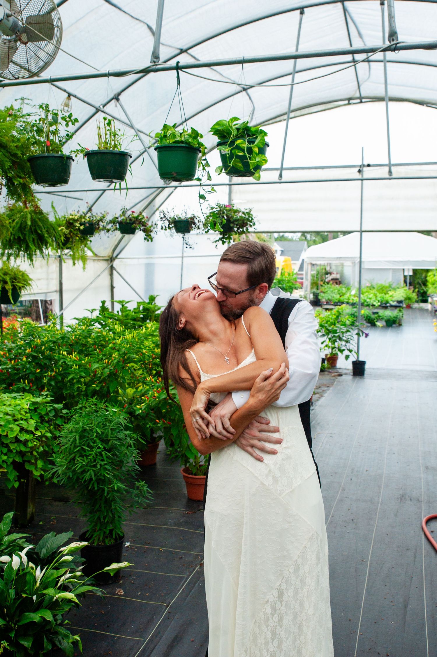 A romantic moment shared between a couple in a greenhouse filled with lush hanging plants and greenery.